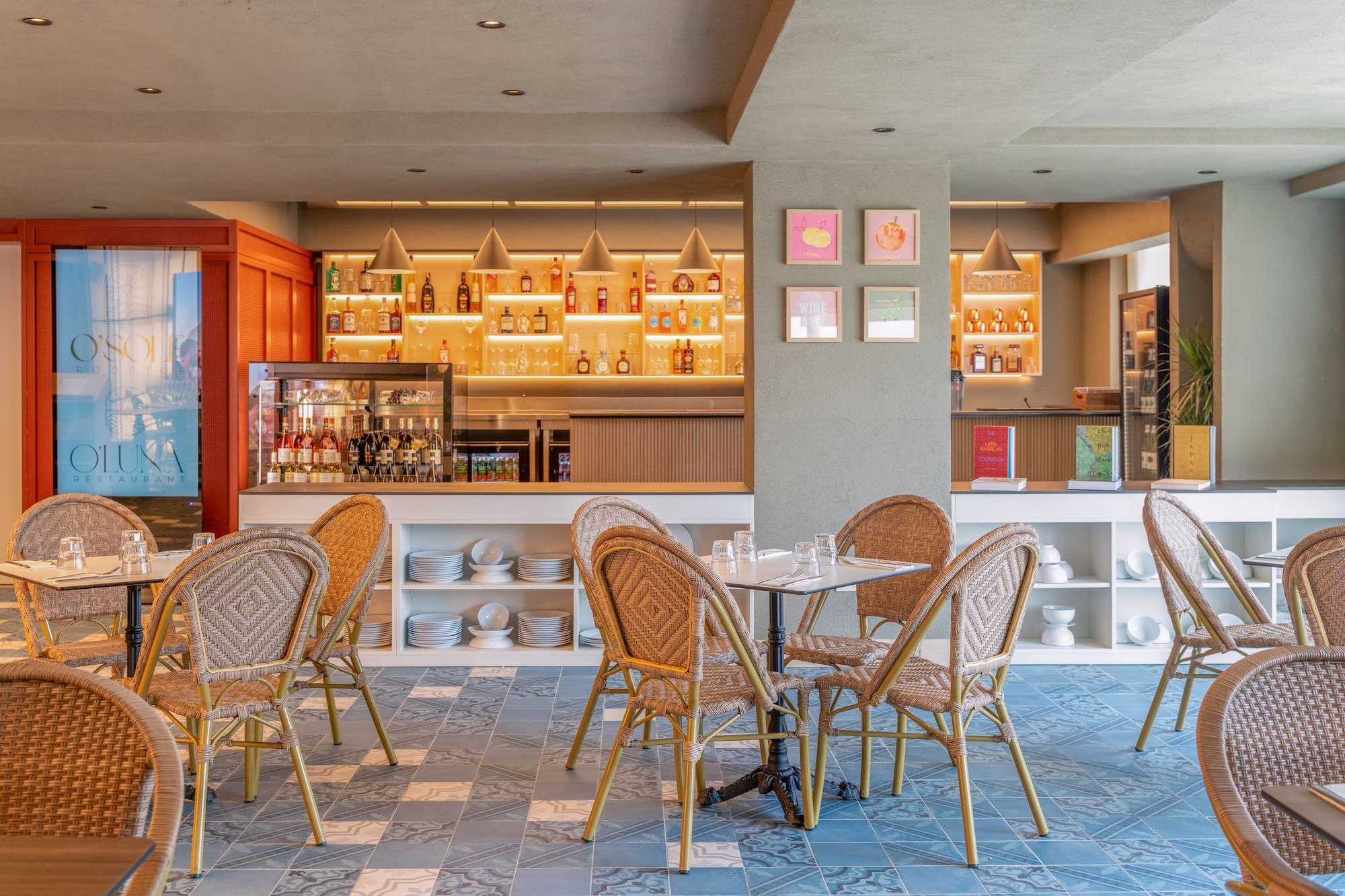 Restaurant dining room with illuminated bar, wicker chairs, and blue patterned floor.