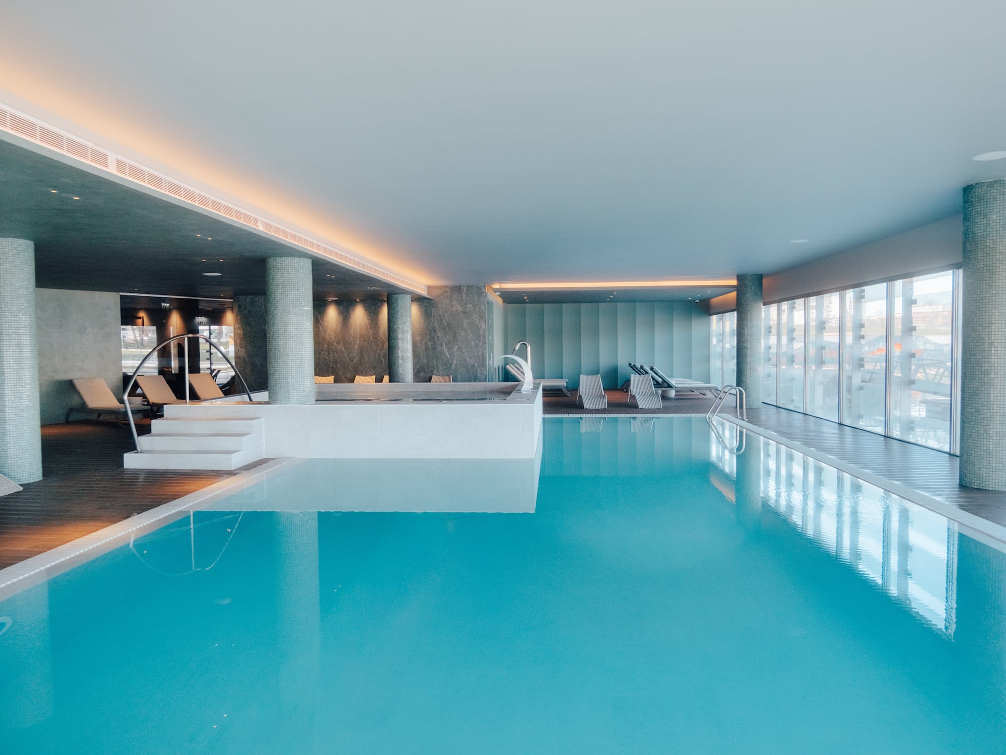 Modern indoor swimming pool with lounge chairs and jacuzzi.