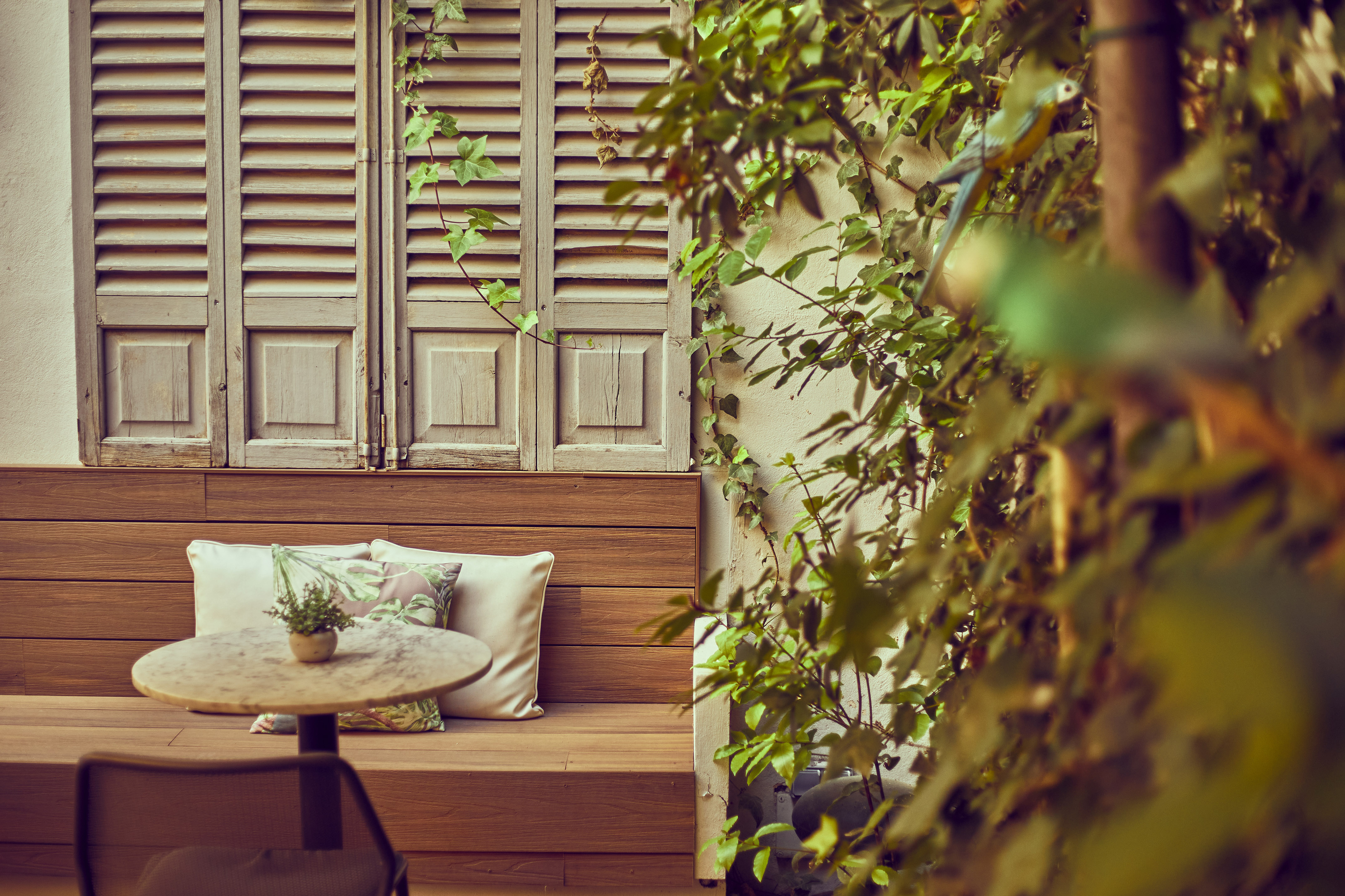 Cozy outdoor patio with wooden bench, marble table, old shutters, and lush ivy.