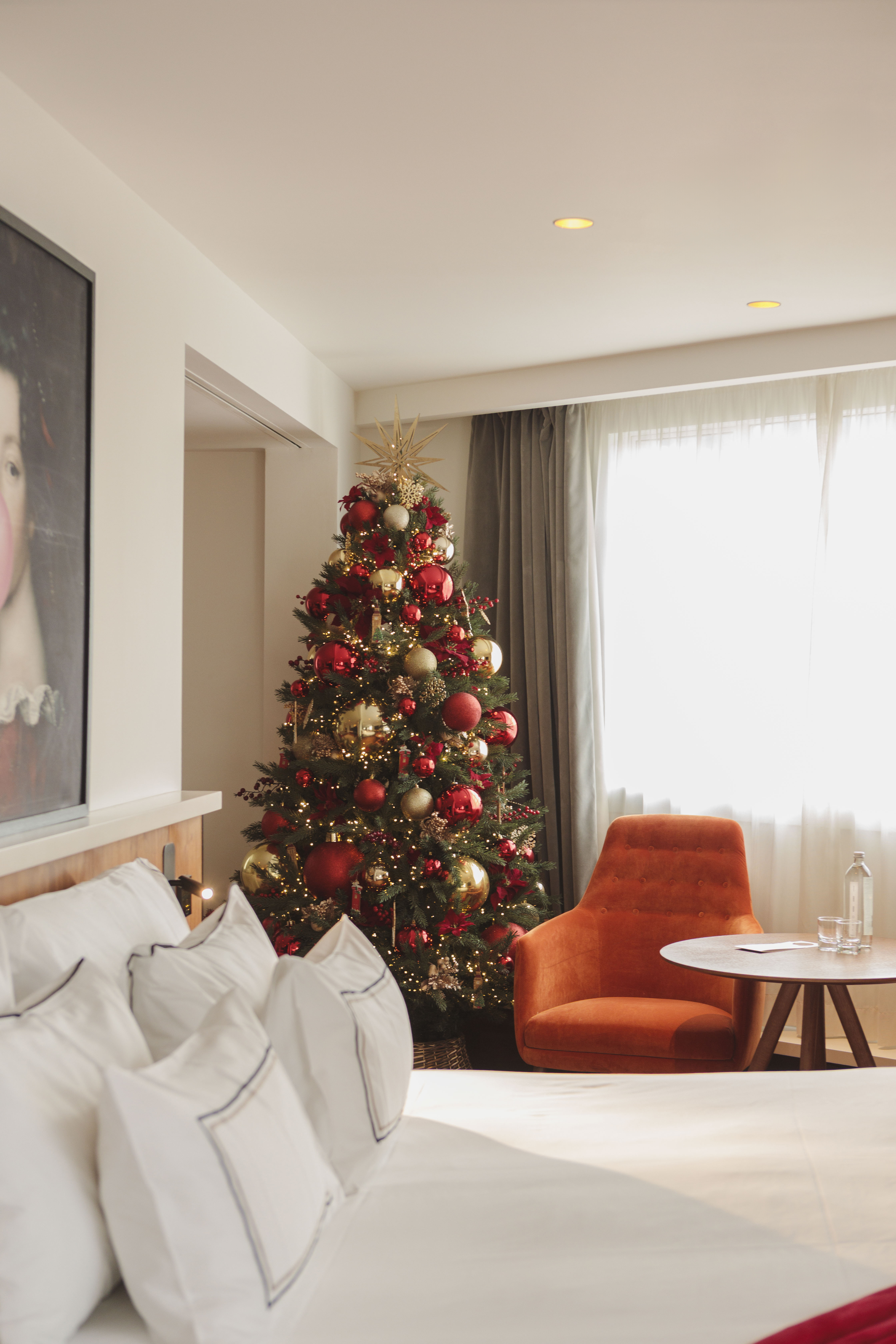Festive Christmas tree with red and gold ornaments in a cozy hotel bedroom.