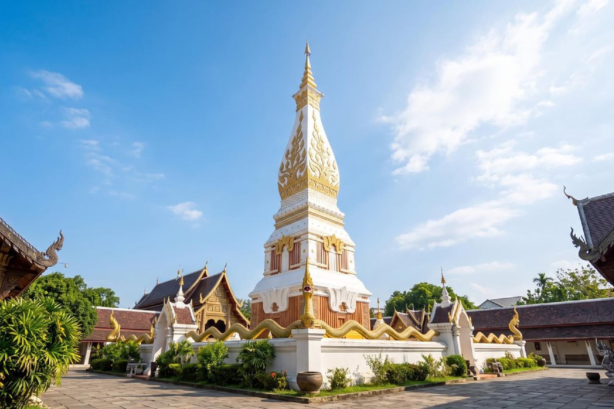 White and gold Thai temple stupa with Naga sculpture under blue sky.