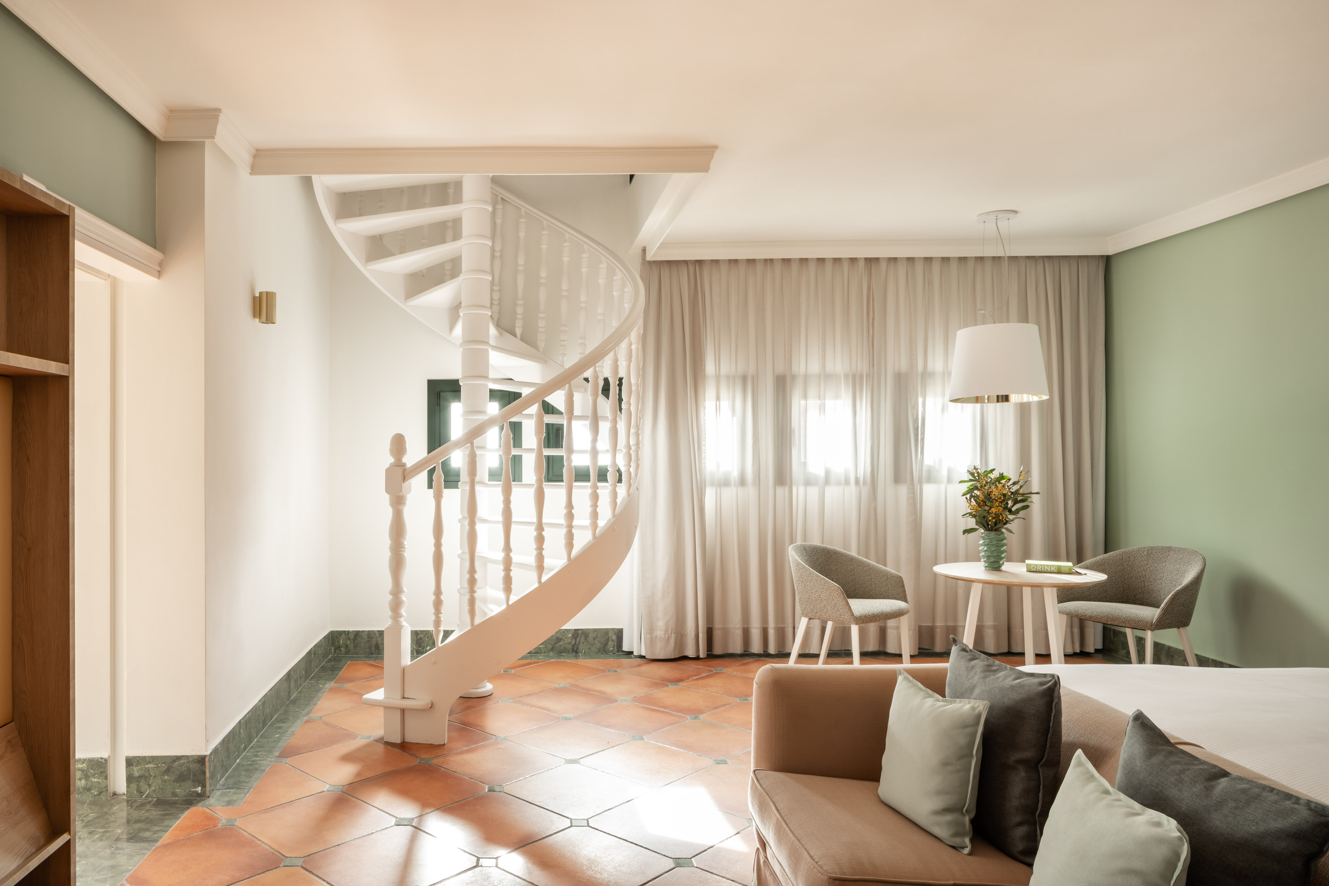 Cozy hotel room with white spiral staircase, terracotta floor, and modern furnishings.