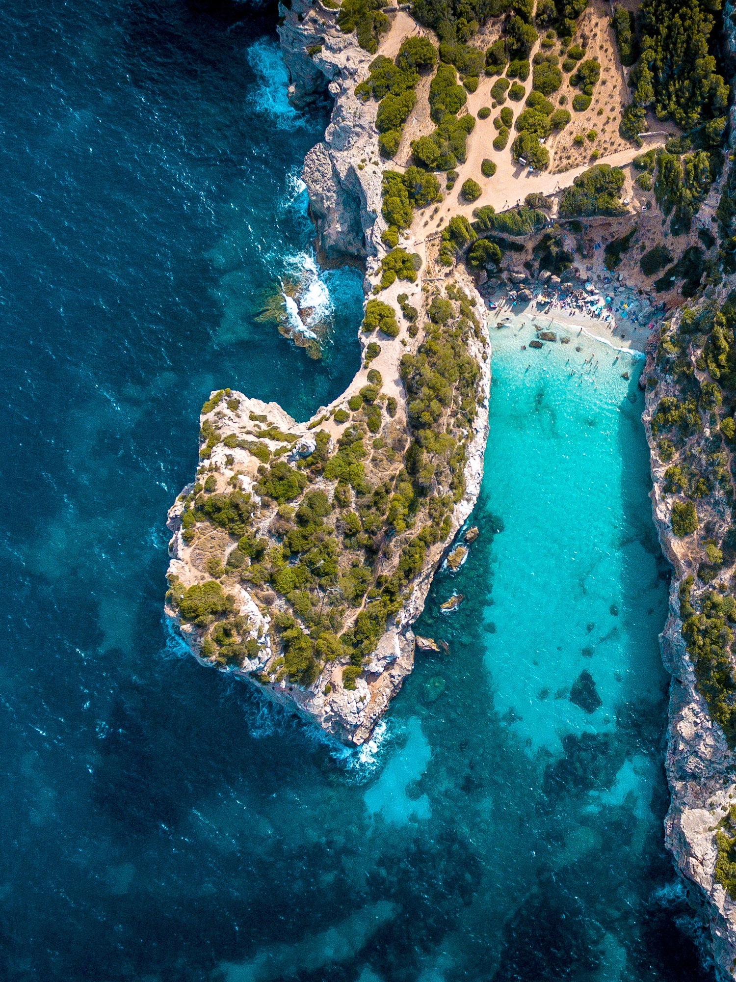 Vista aérea: Cala con playa de arena, acantilados y mar turquesa.
