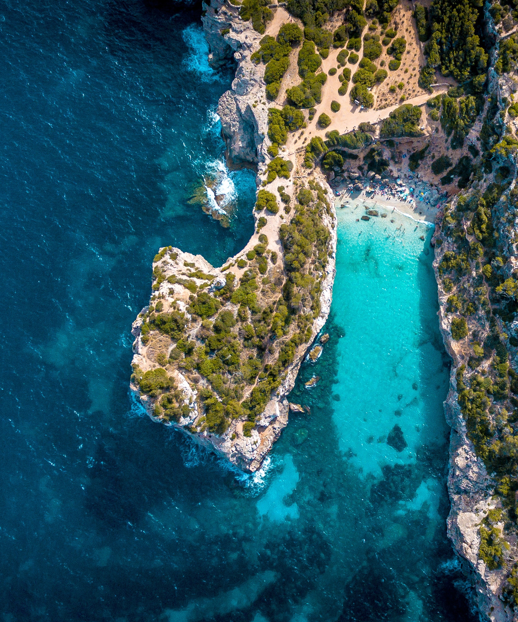 Vista aérea: Cala con playa de arena, acantilados y mar turquesa.