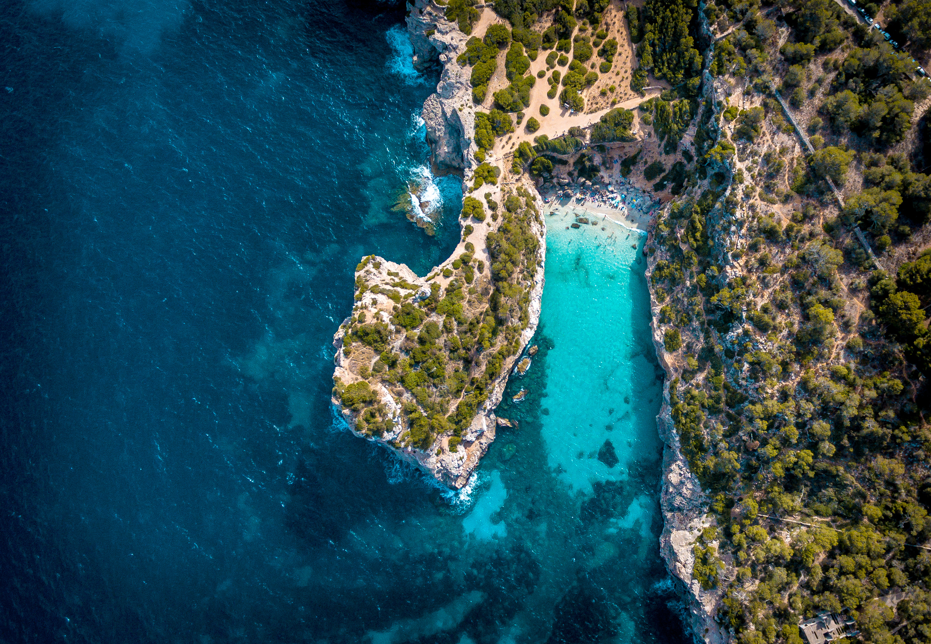 Vista aérea: Cala con playa de arena, acantilados y mar turquesa.