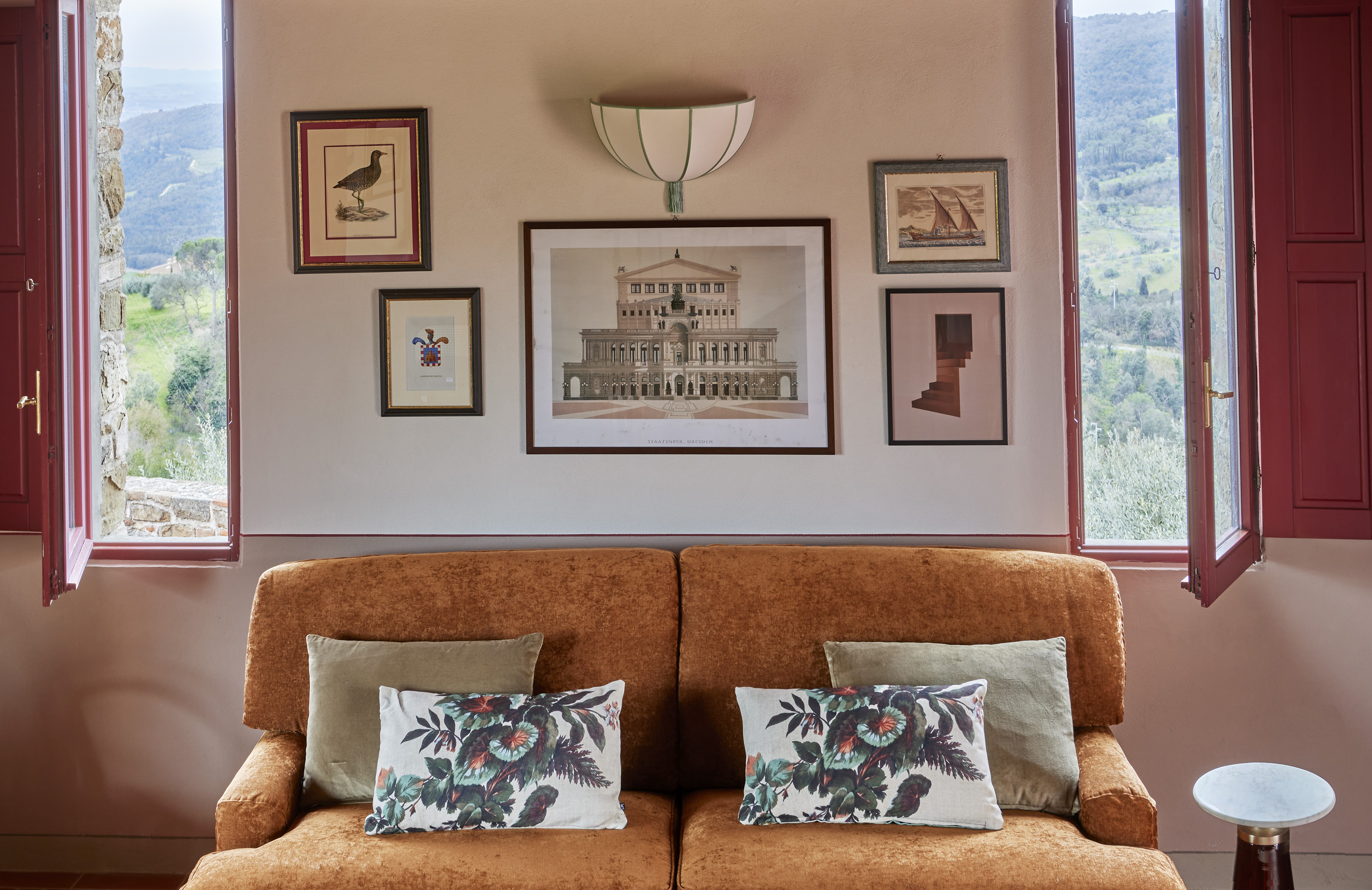 Rust velvet sofa, gallery wall with varied art, and open windows to a scenic valley.