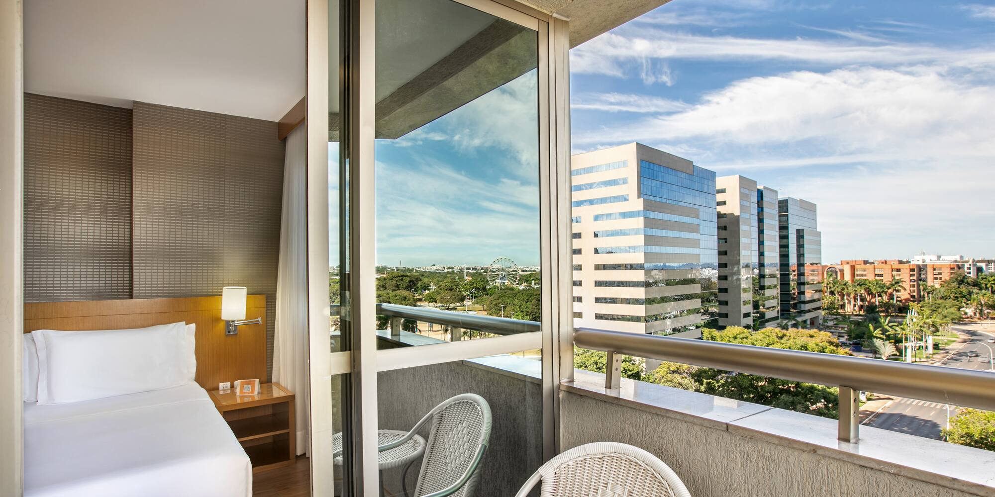 Hotel room with private balcony, city skyline, and distant Ferris wheel.