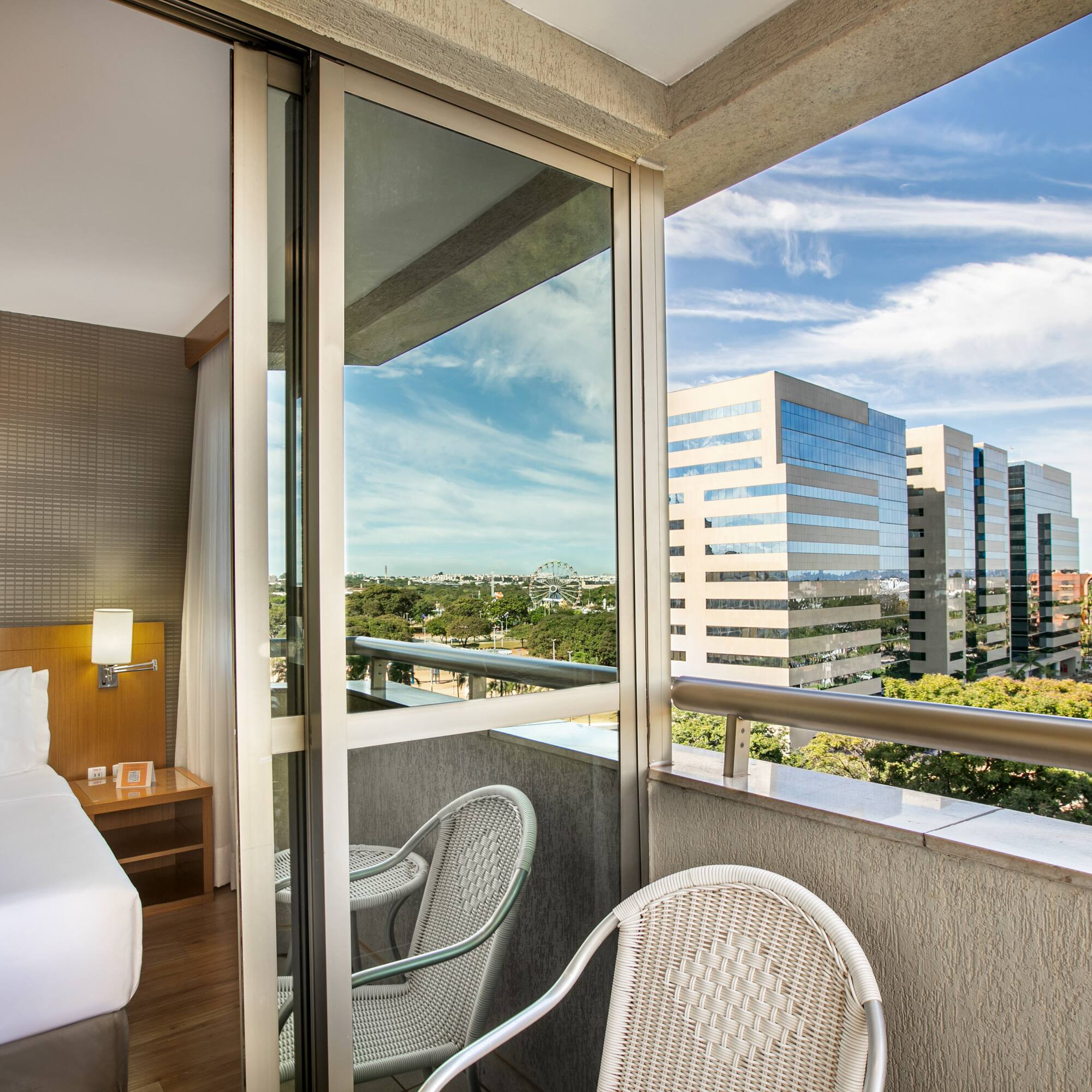 Hotel room with private balcony, city skyline, and distant Ferris wheel.