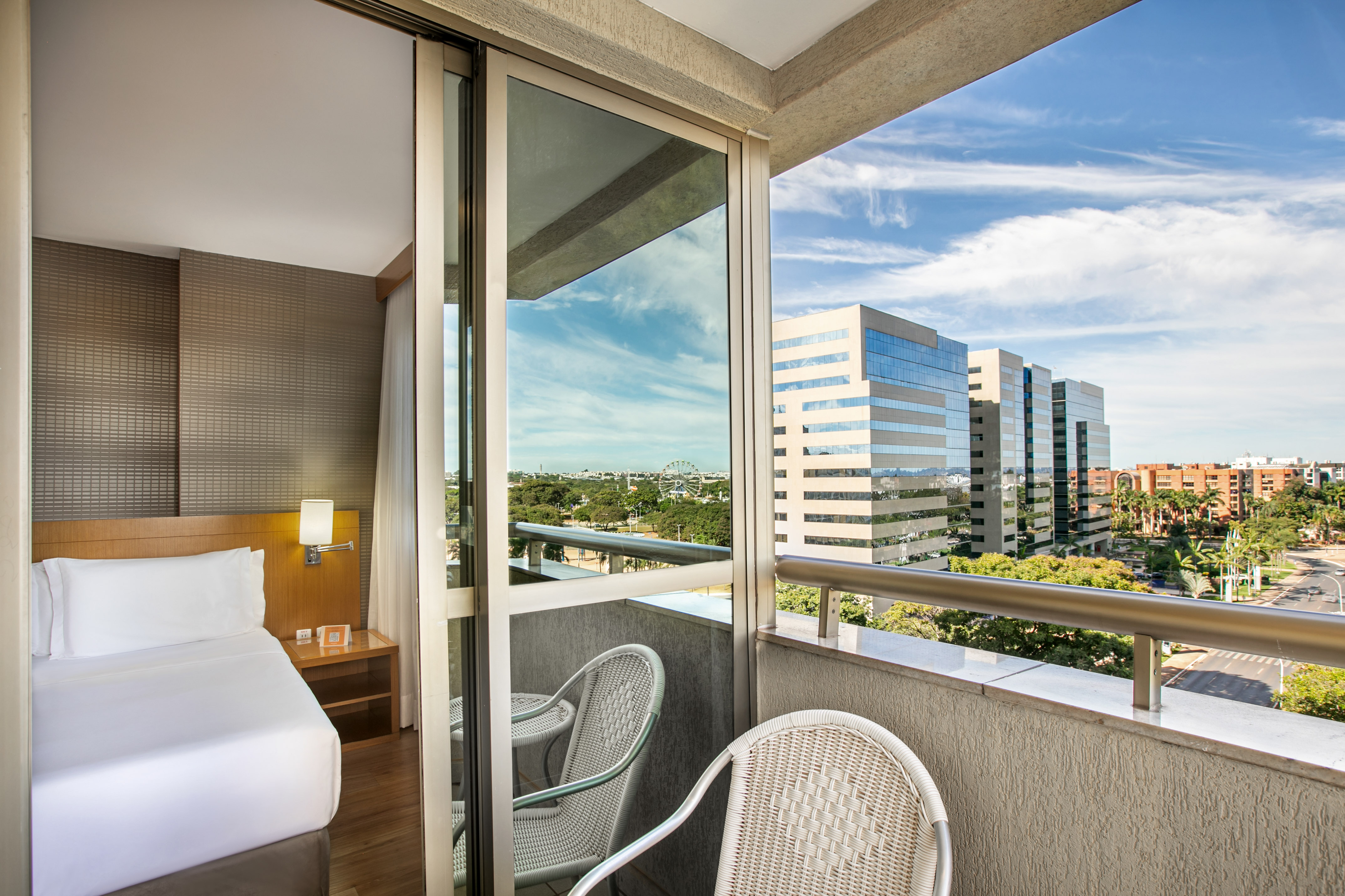Hotel room with private balcony, city skyline, and distant Ferris wheel.