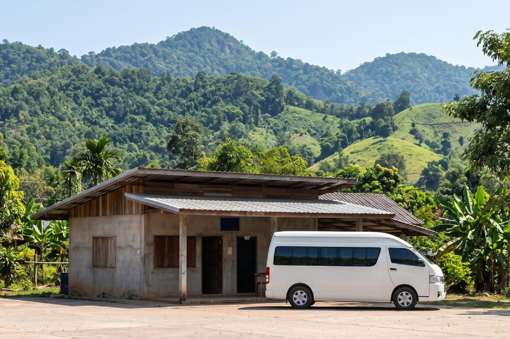 White minibus parked at a rural rest stop, tropical mountains behind.