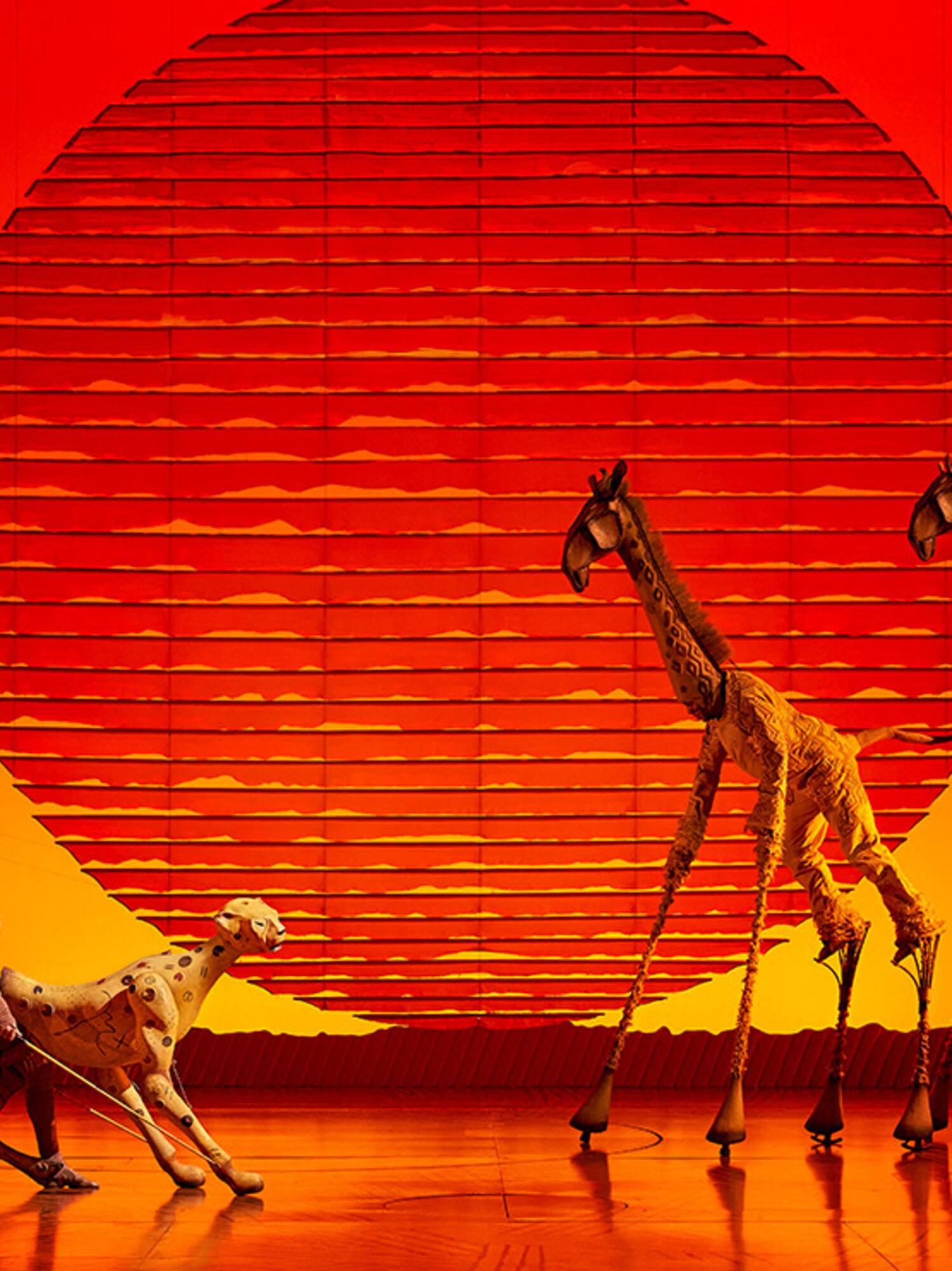 The Lion King musical stage with giraffe puppets and cheetah costume, red sunset.
