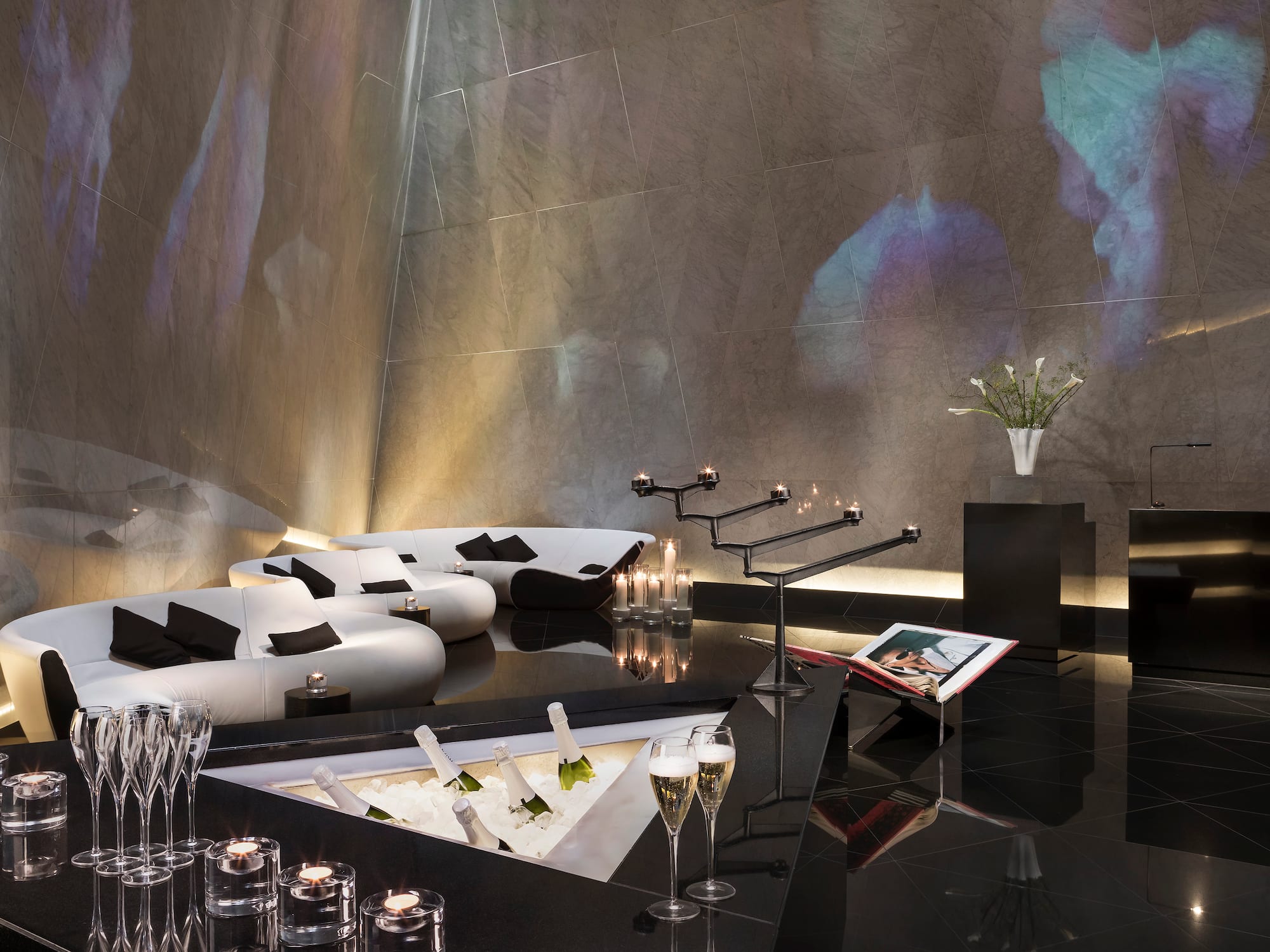 A room featuring a black floor, white couches, and wine glasses.