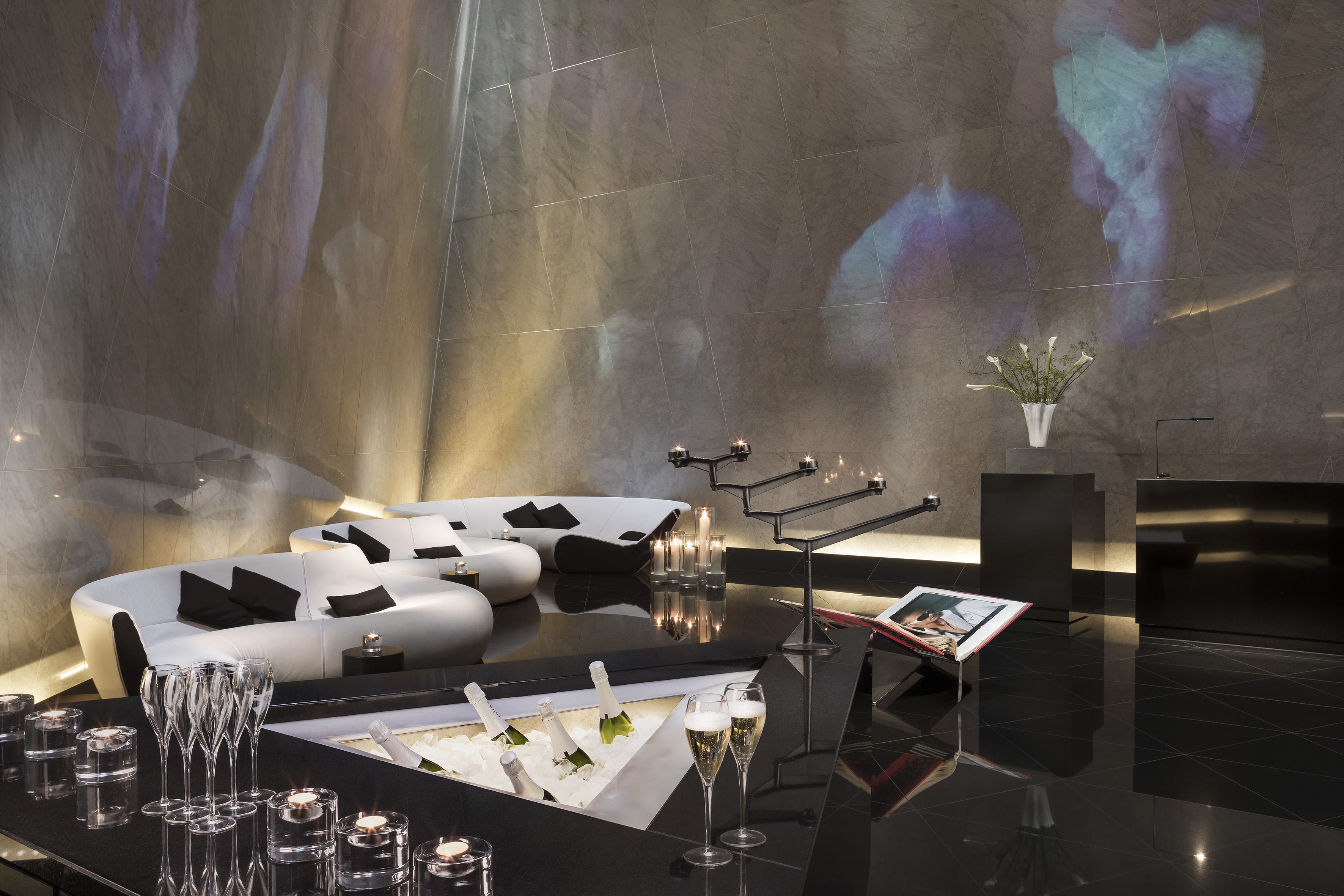 A room featuring a black floor, white couches, and wine glasses.