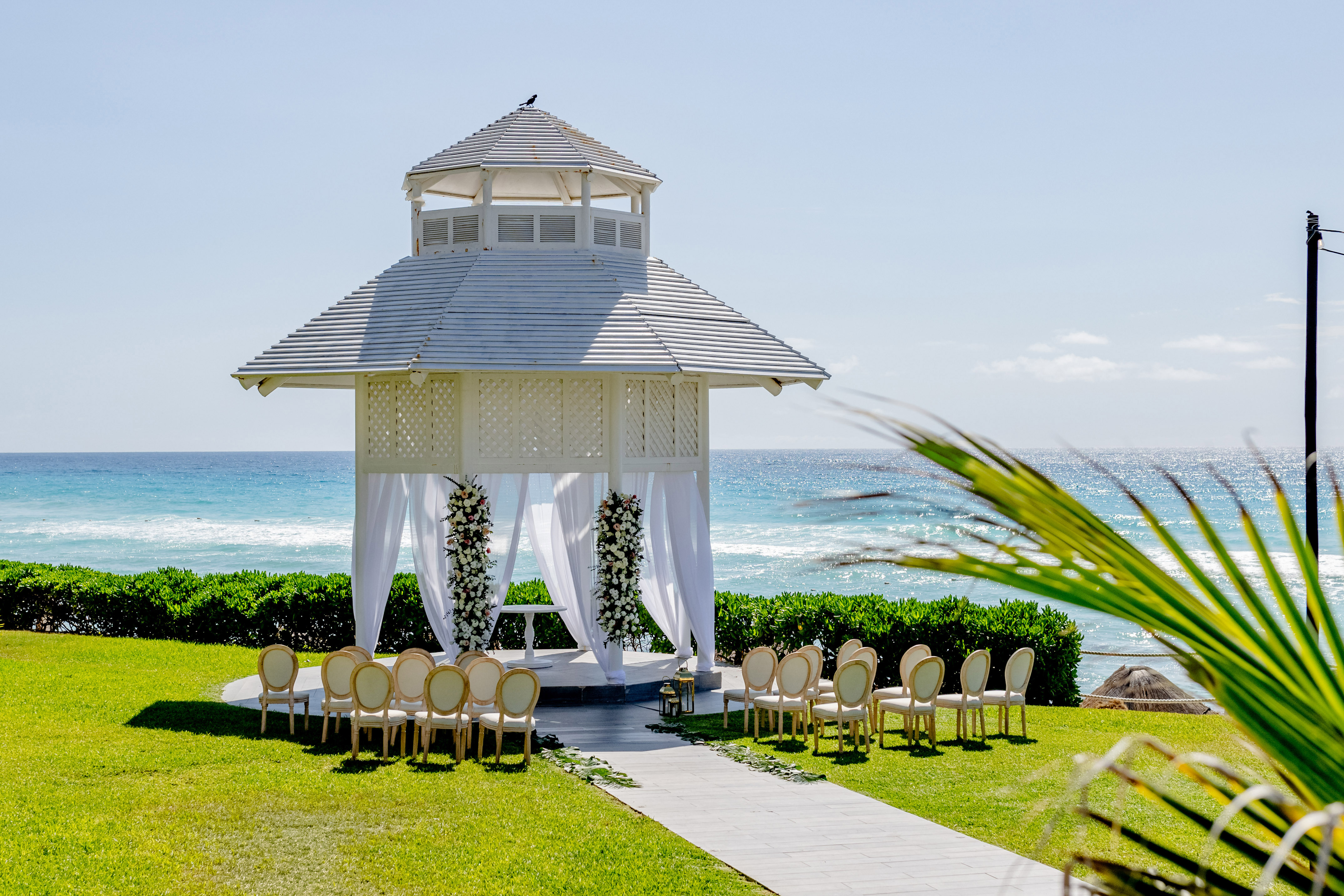 Beach wedding ceremony with white gazebo, chairs, and ocean view.
