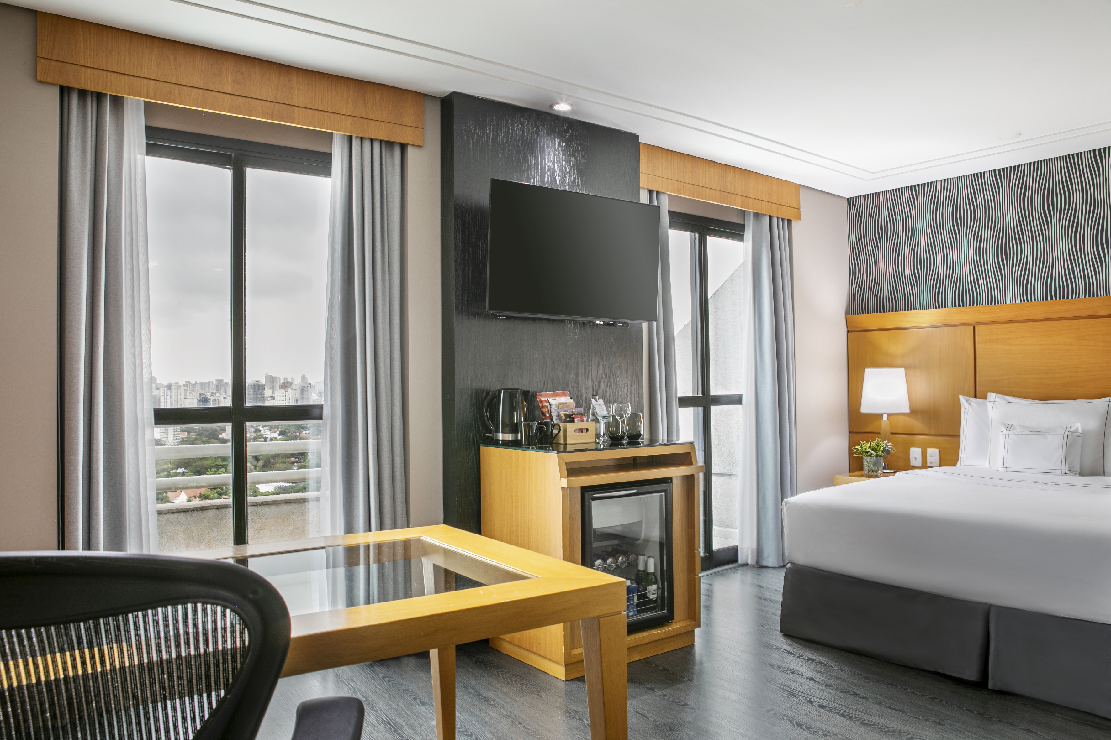Spacious hotel room with bed, desk, TV, minibar, and city view.