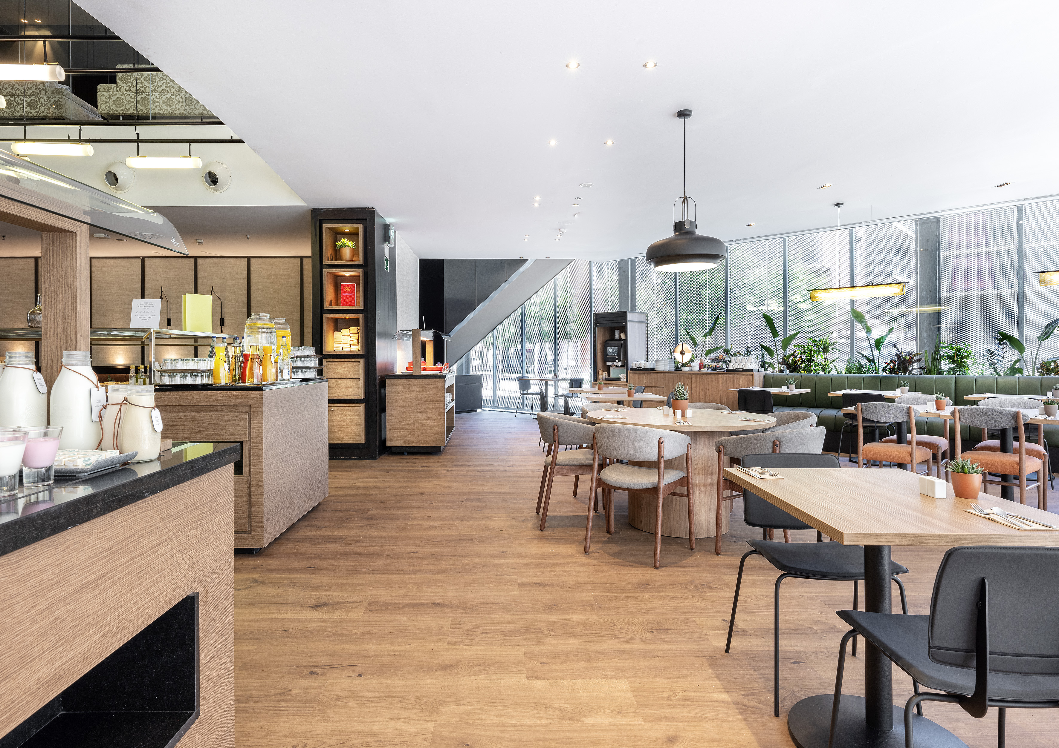 Modern hotel restaurant with breakfast buffet, dining tables, and green plants. - مطعم متوسطي, المطبخ المتوسطي - فندق برشلونة كوندال مار(Condal Mar) المنتسب لـ Melia, برشلونة
