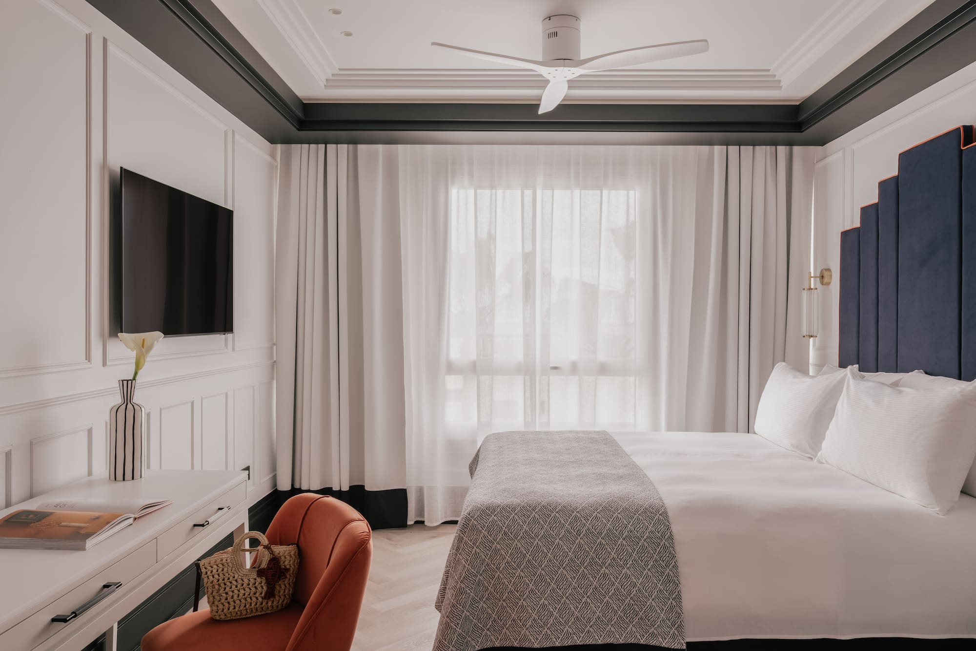 Modern hotel bedroom with white bed, blue headboard, TV, and desk.
