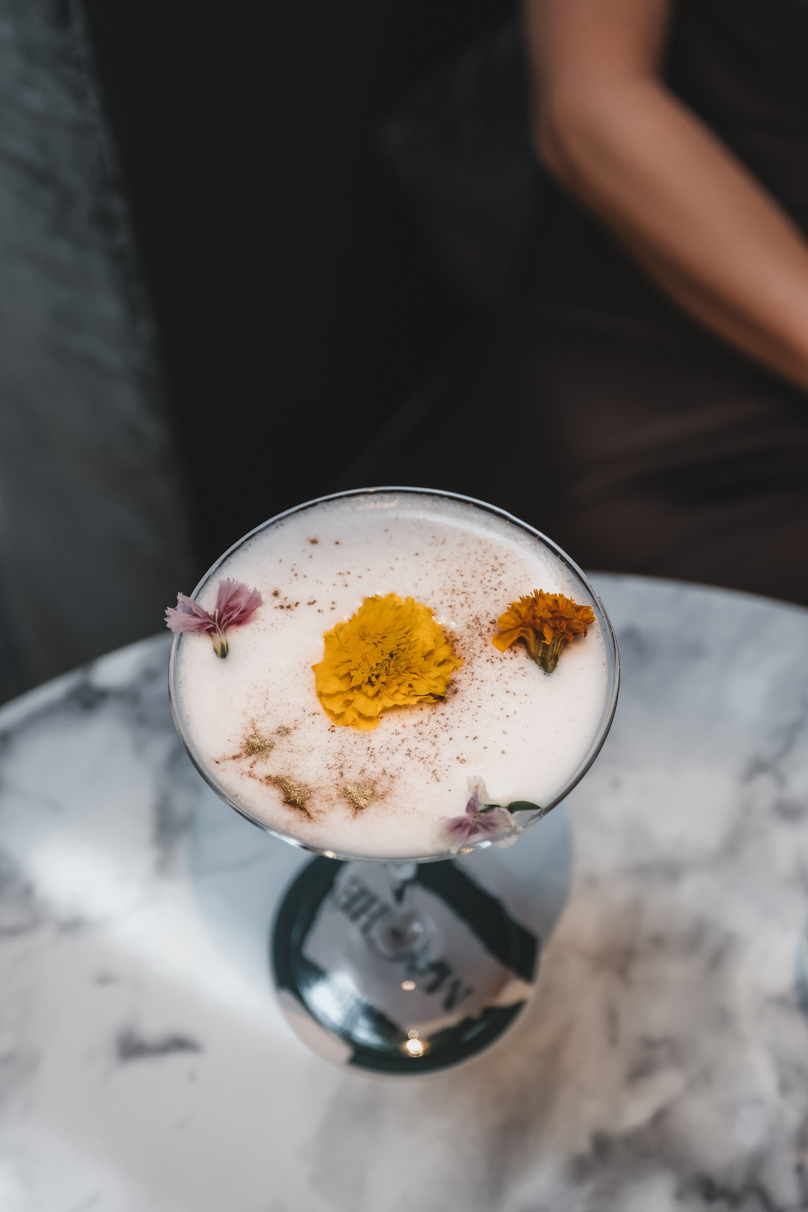 Elegant foamy cocktail with edible flowers and gold dust on marble table.