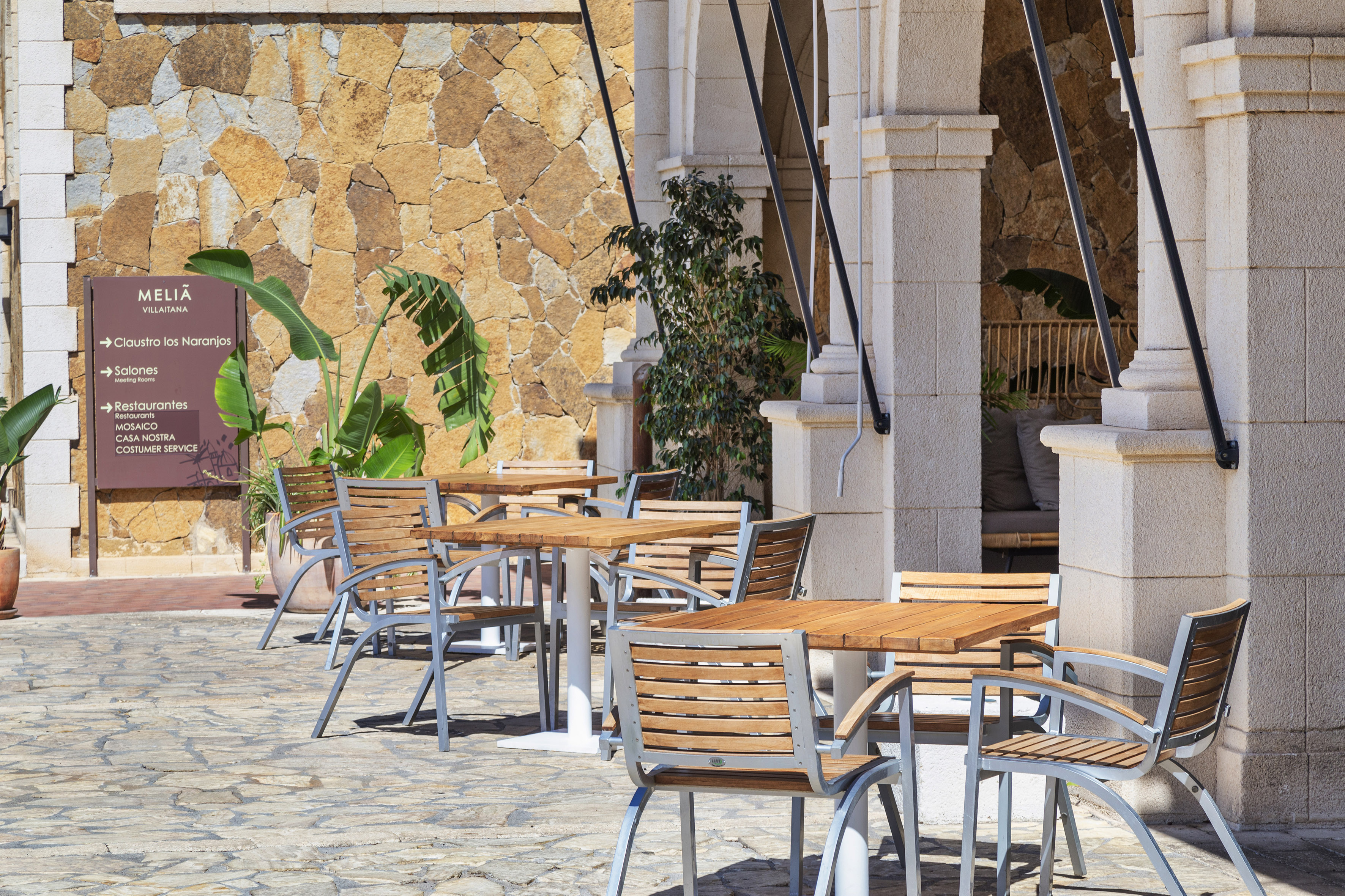 Meliá Villaitana restaurant patio with wooden tables, stone wall, and plants.