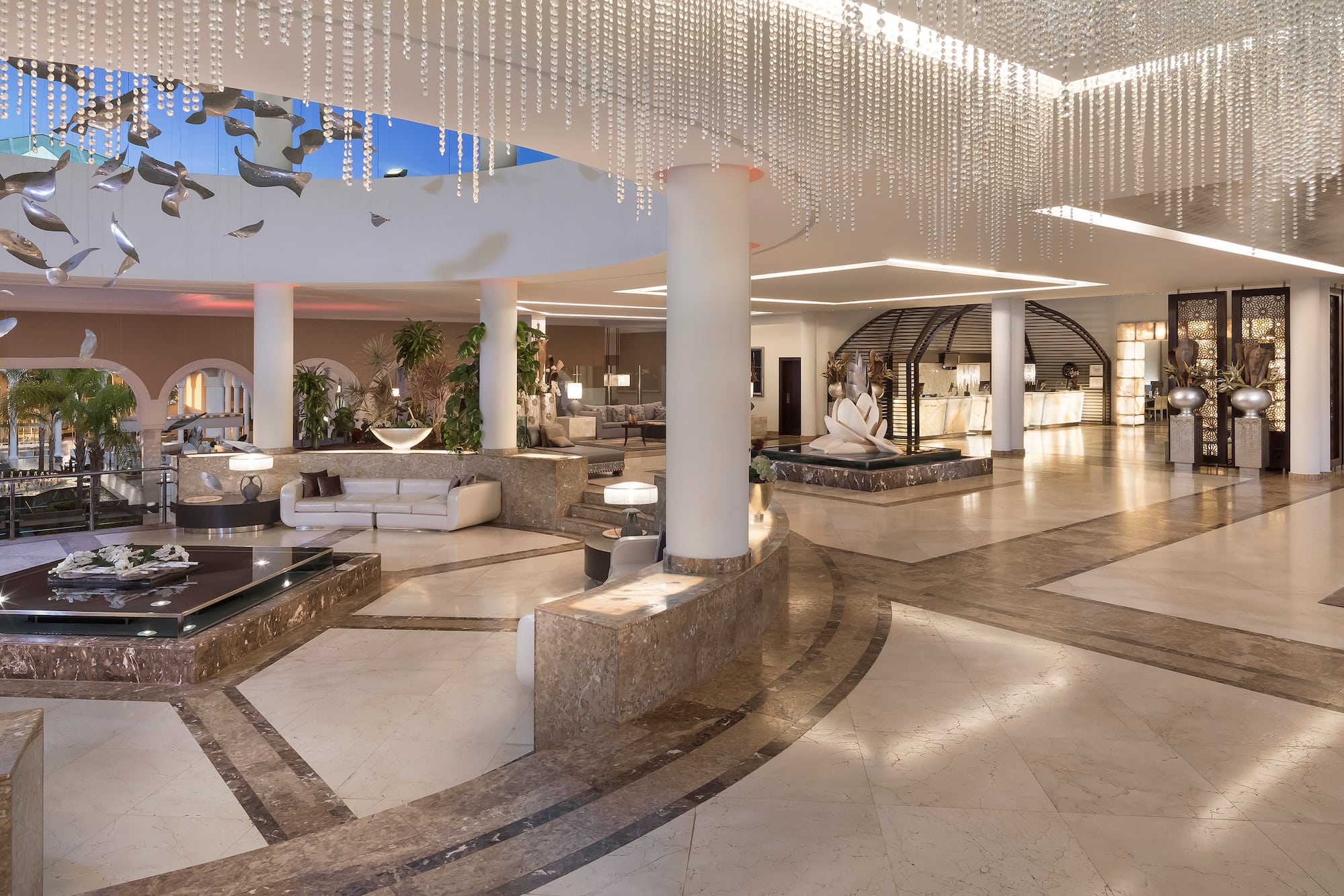 Spacious luxury hotel lobby with crystal chandeliers, marble floor, modern seating, fountain.