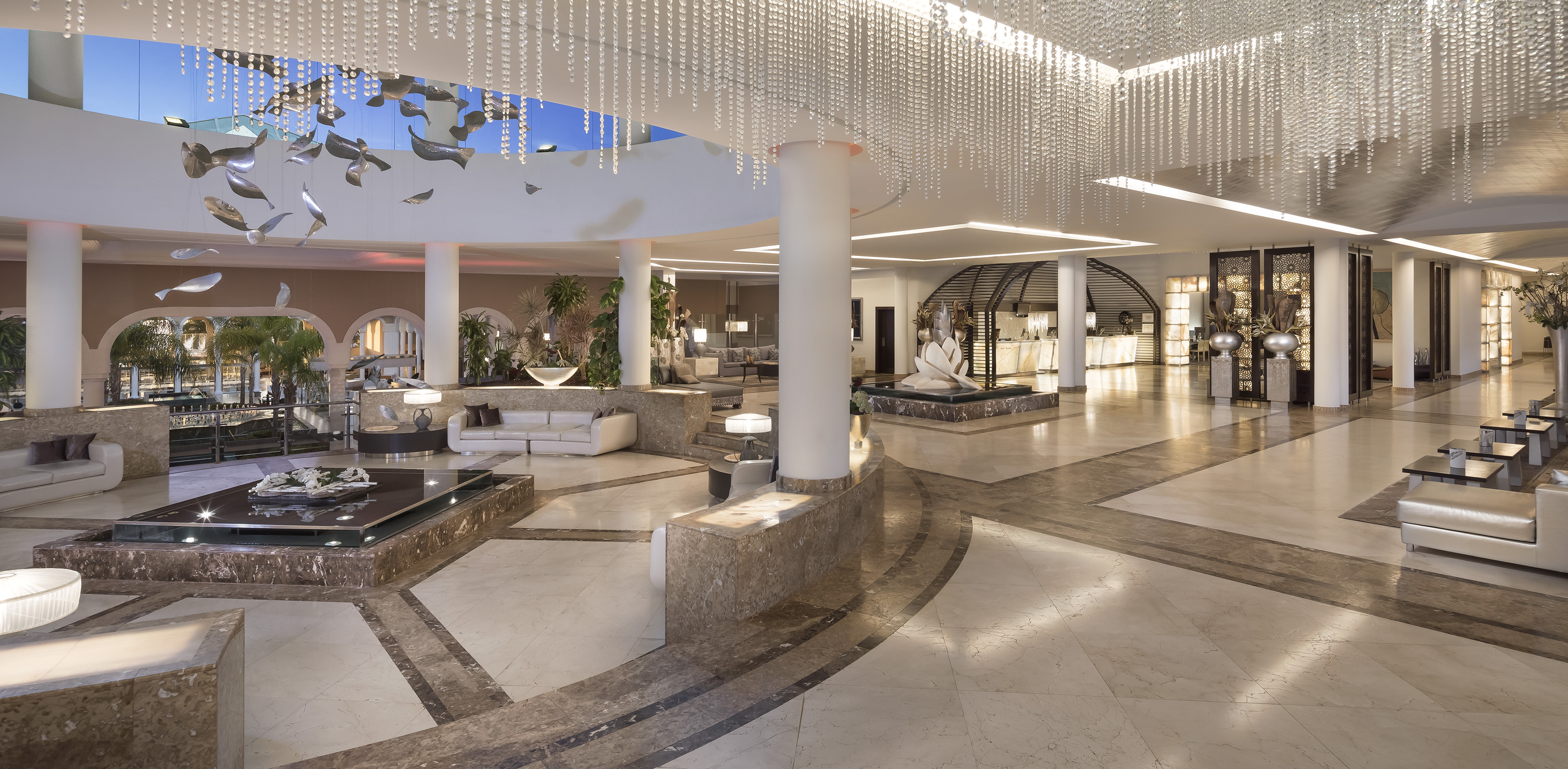 Spacious luxury hotel lobby with crystal chandeliers, marble floor, modern seating, fountain.