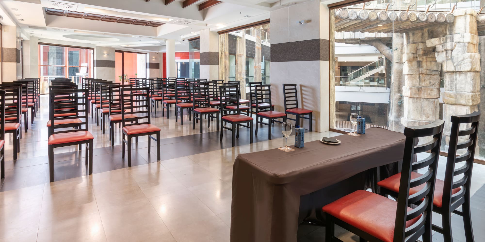 Meeting room with rows of red chairs, a presentation table, and large windows.