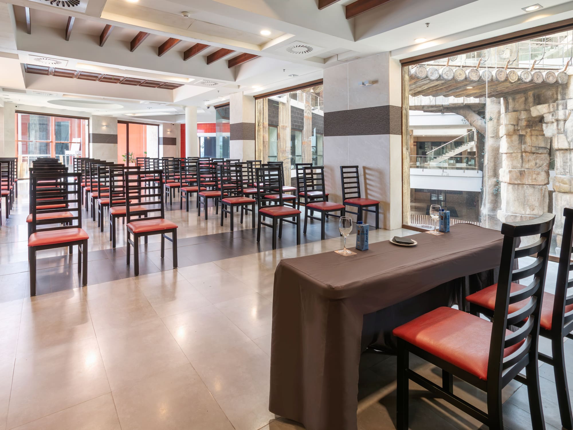 Event venue classroom setup with red chairs, presentation table, large windows.