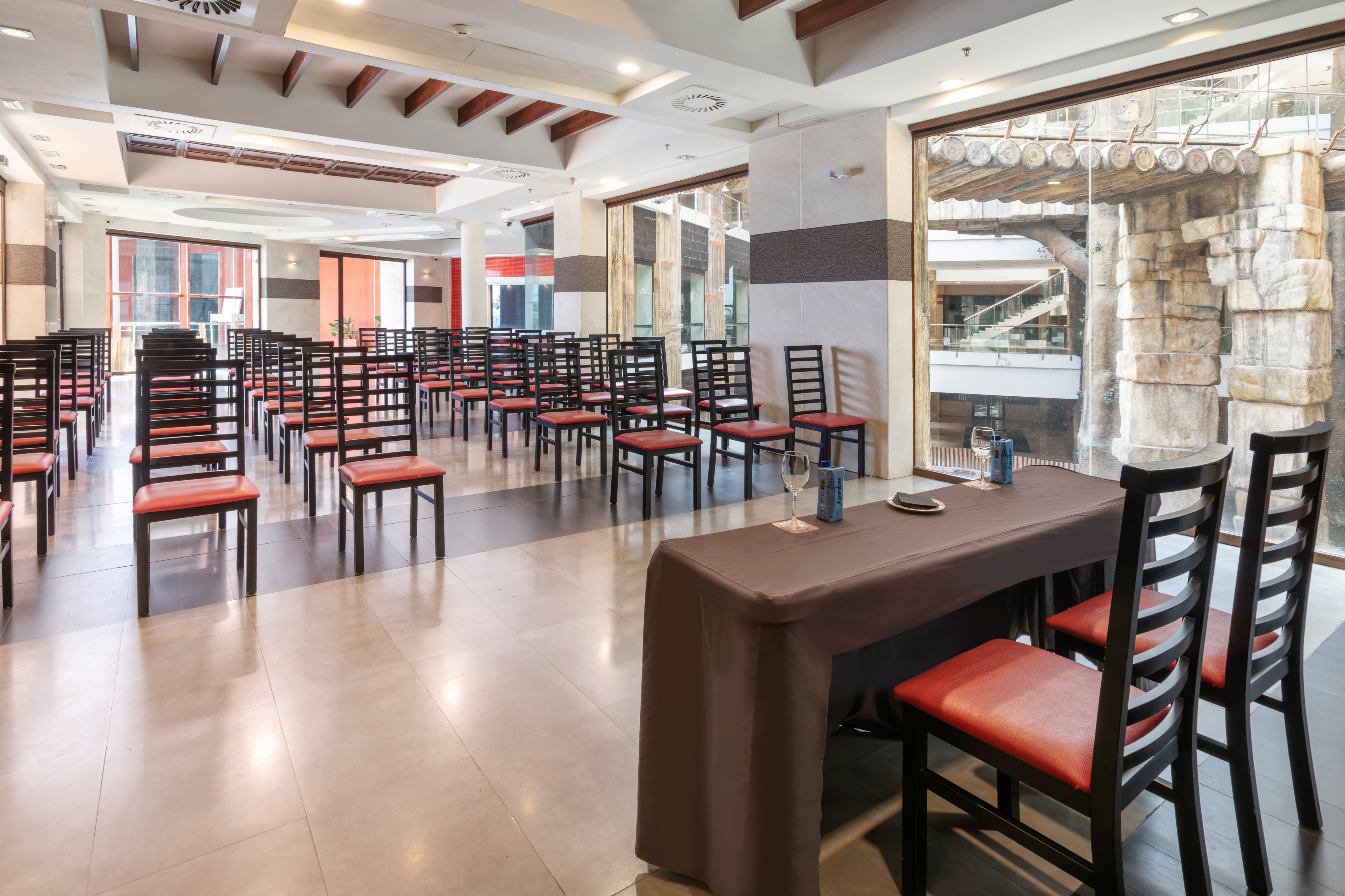 Meeting room with rows of red chairs, a presentation table, and large windows.