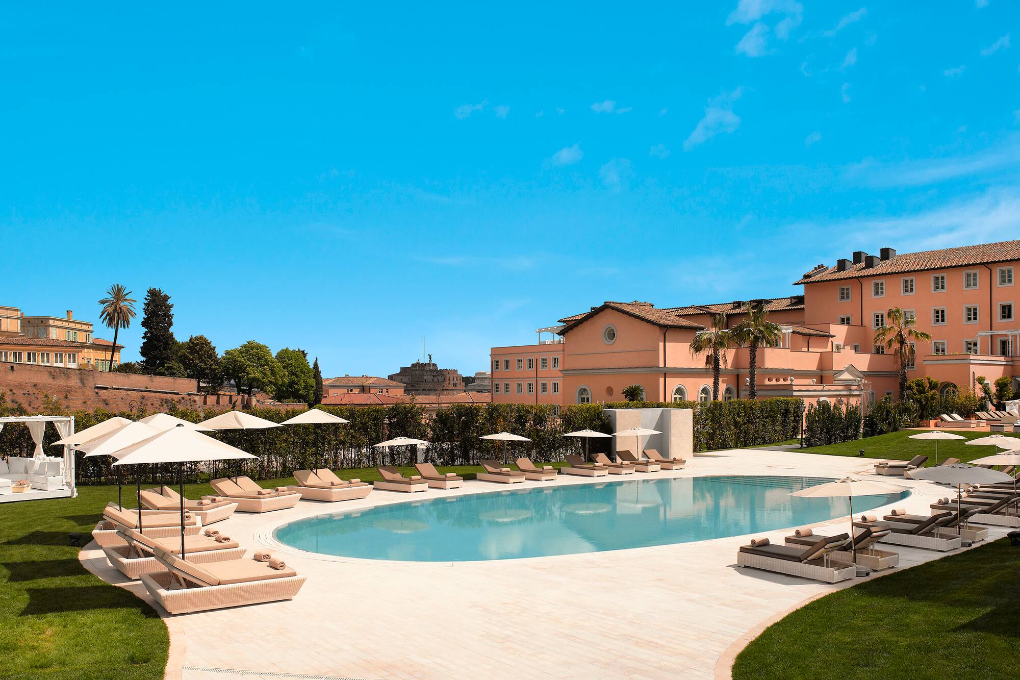Rome resort pool with sun loungers, umbrellas, and historic buildings.