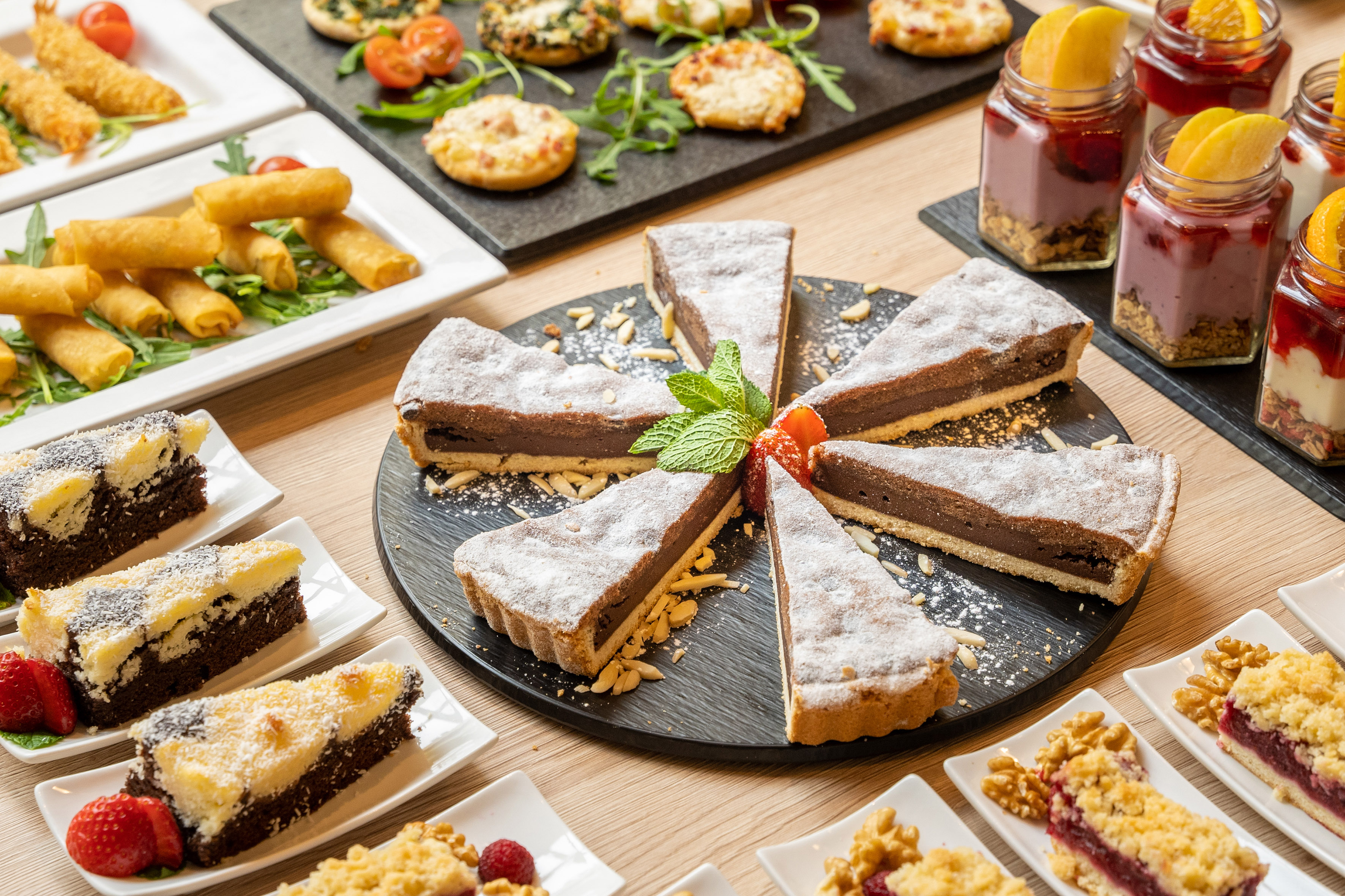 Buffet of chocolate tart, mini cakes, parfaits, and savory appetizers.