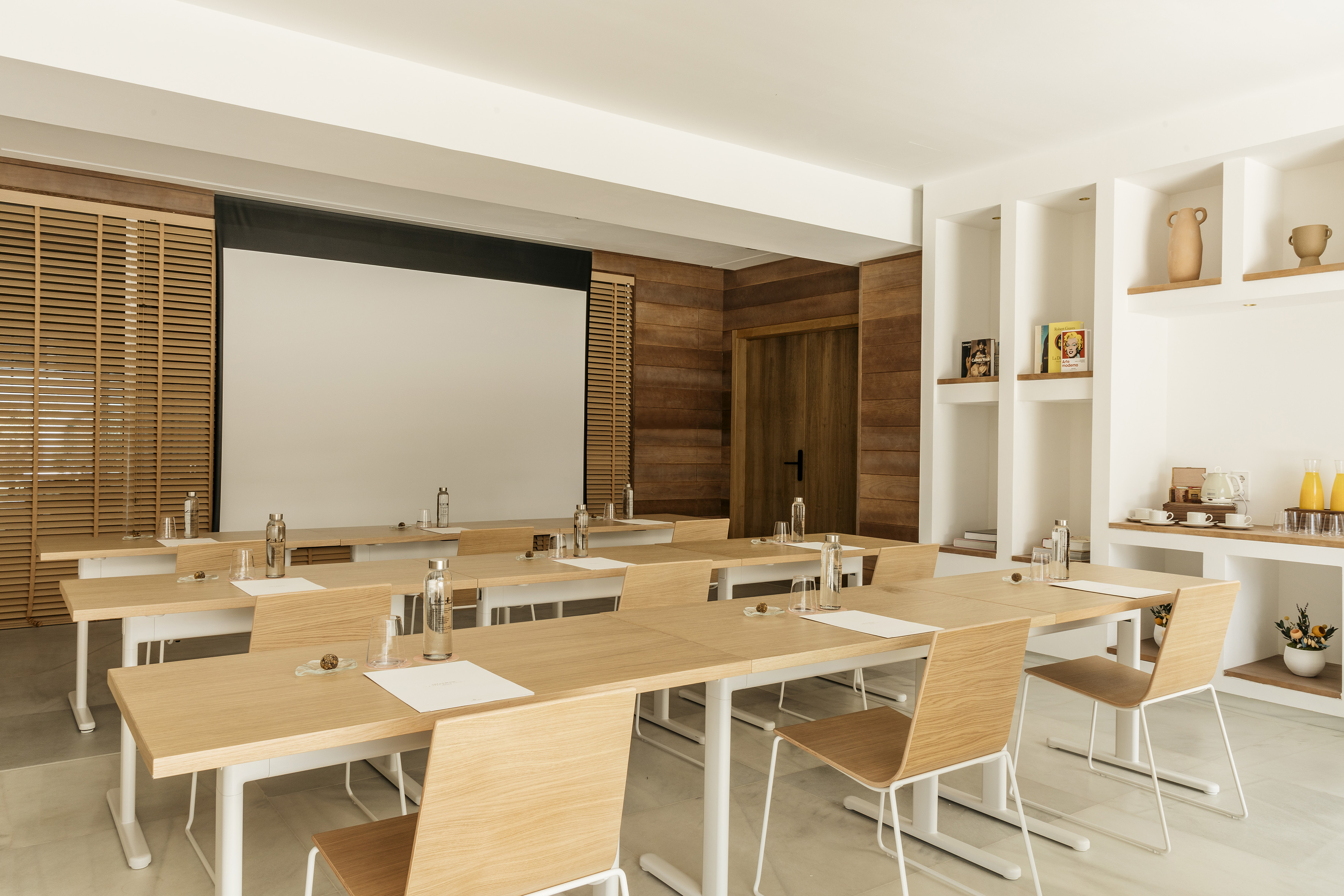 Modern meeting room with light wood furniture and large projection screen.