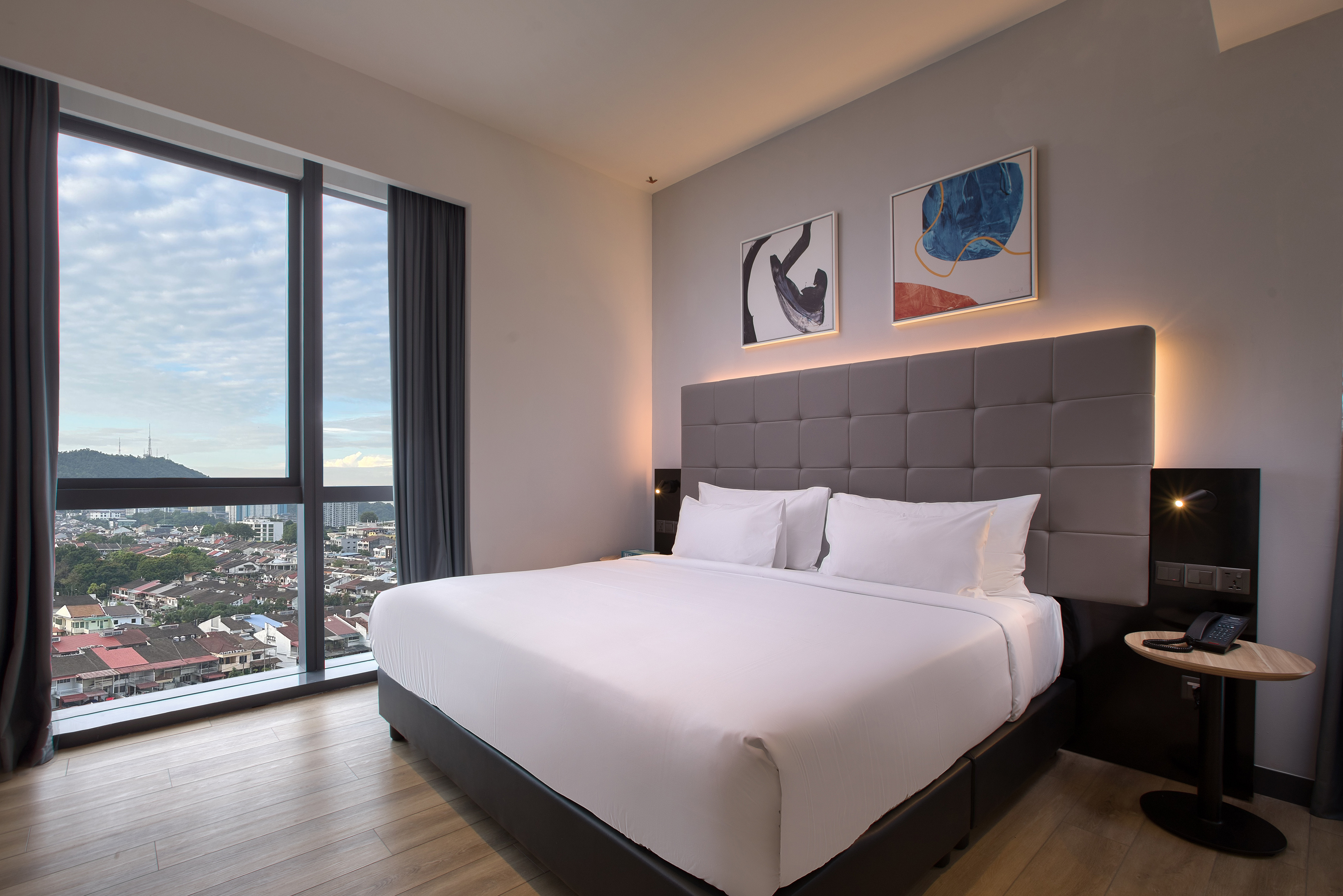 Spacious hotel bedroom with king bed, city view window, modern decor.