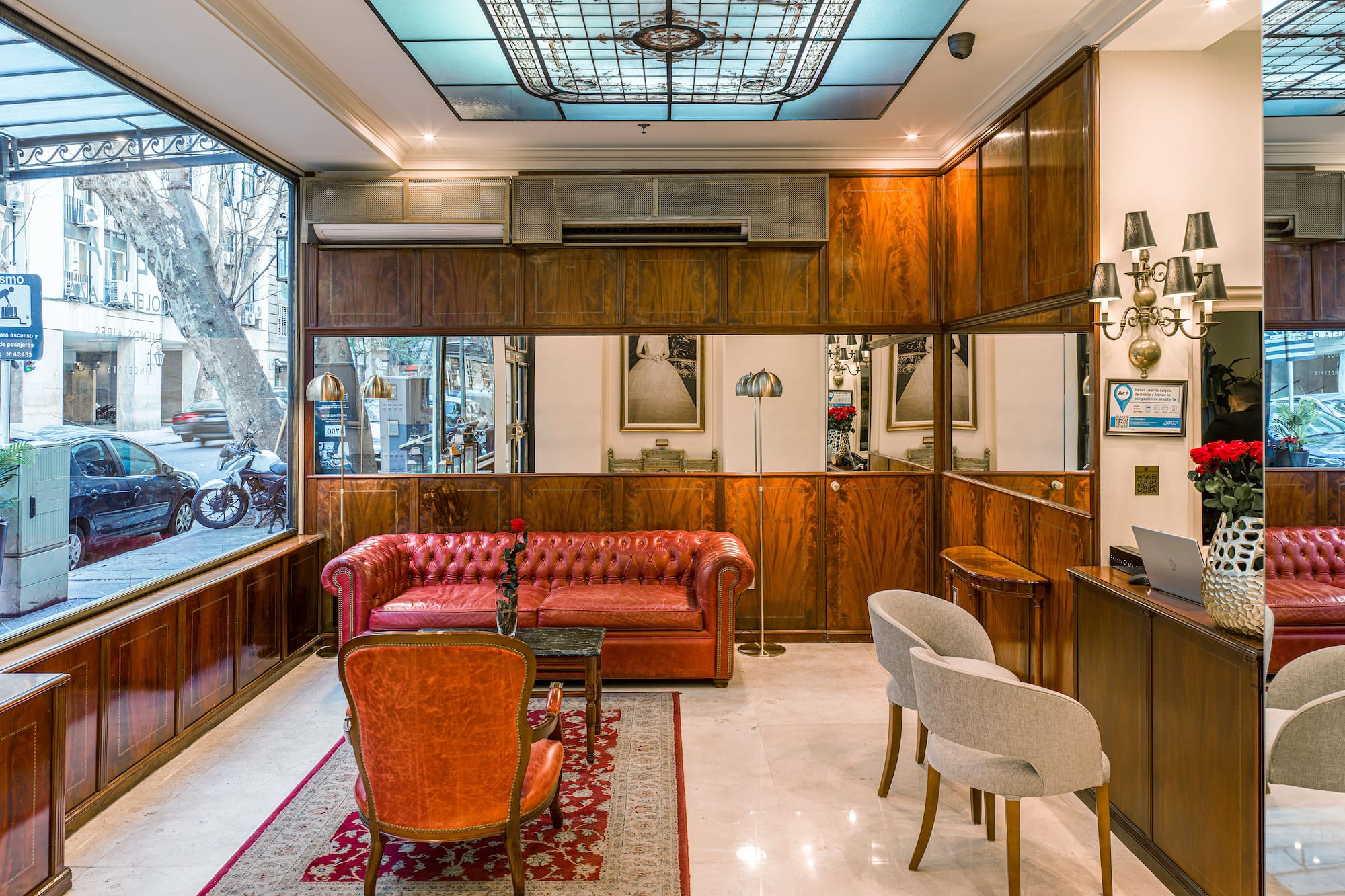 Luxurious hotel lobby with red Chesterfield sofa, wooden panels, stained glass ceiling.