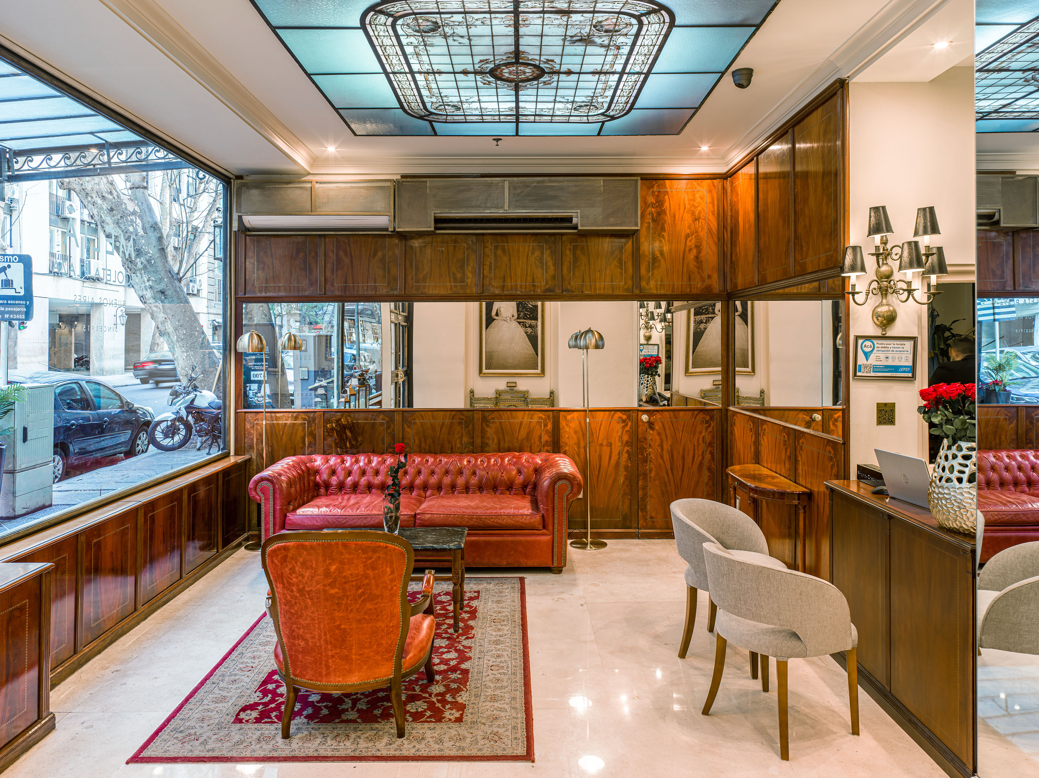 Luxurious hotel lobby with red Chesterfield sofa, wooden panels, stained glass ceiling.