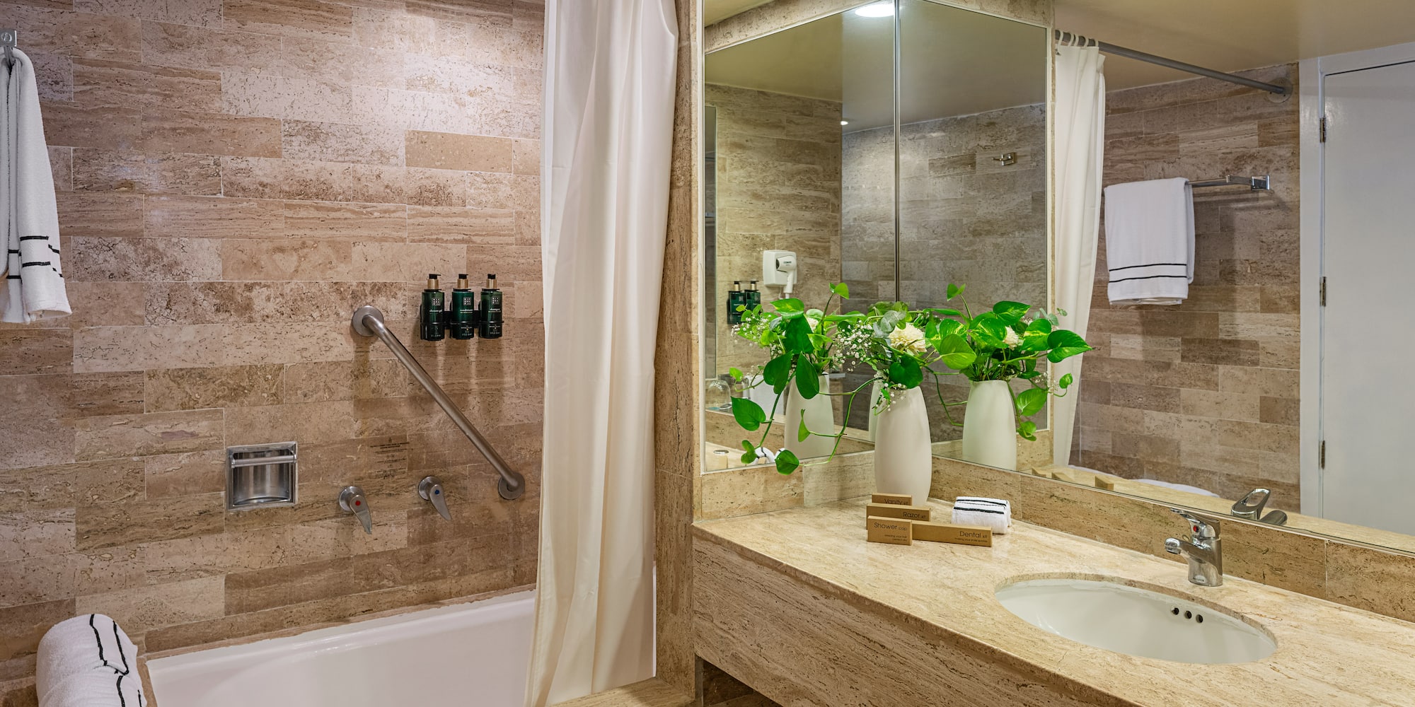 Stylish hotel bathroom with travertine tile, bathtub, grab bar, and vanity.
