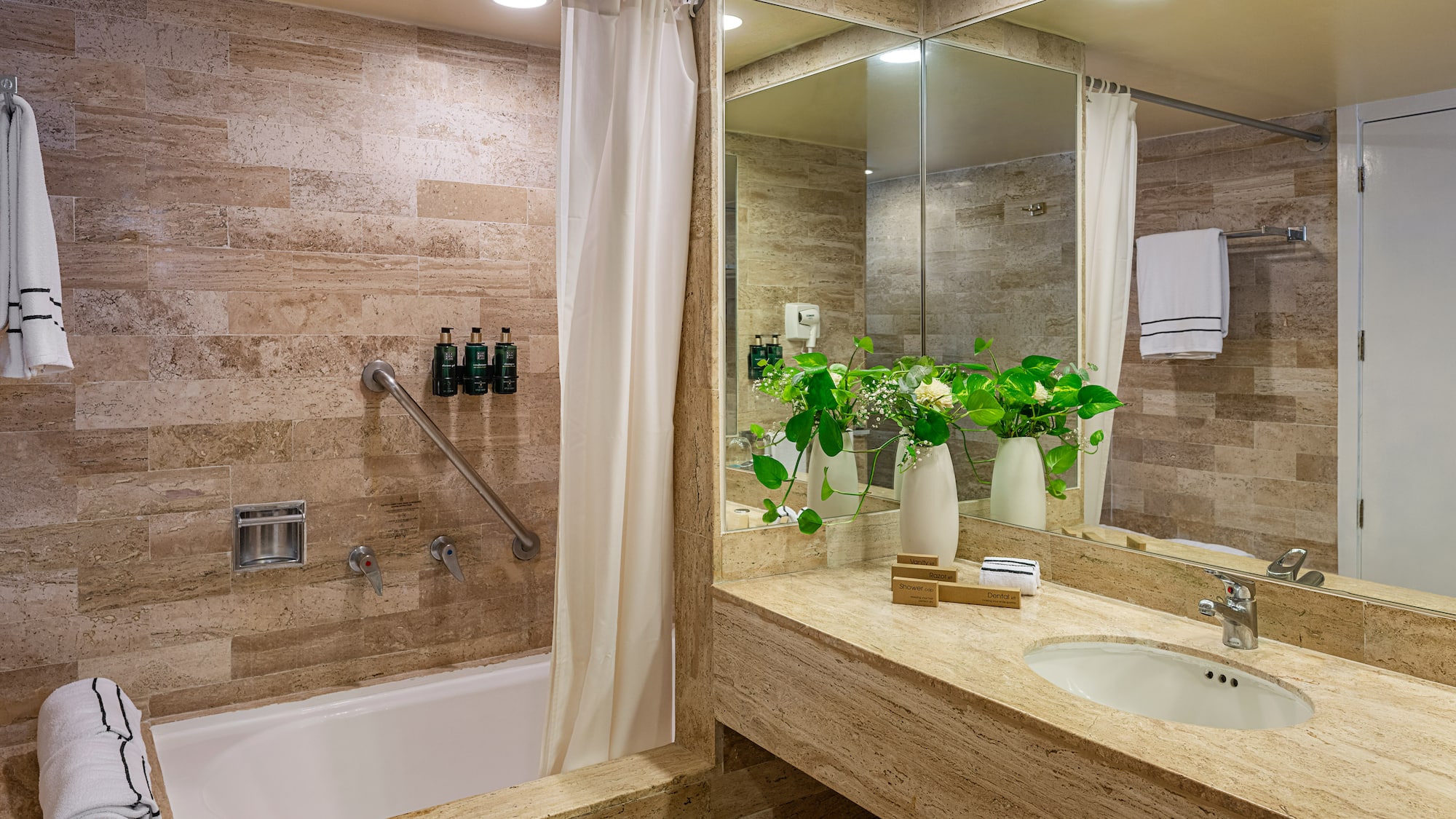 Stylish hotel bathroom with travertine tile, bathtub, grab bar, and vanity.