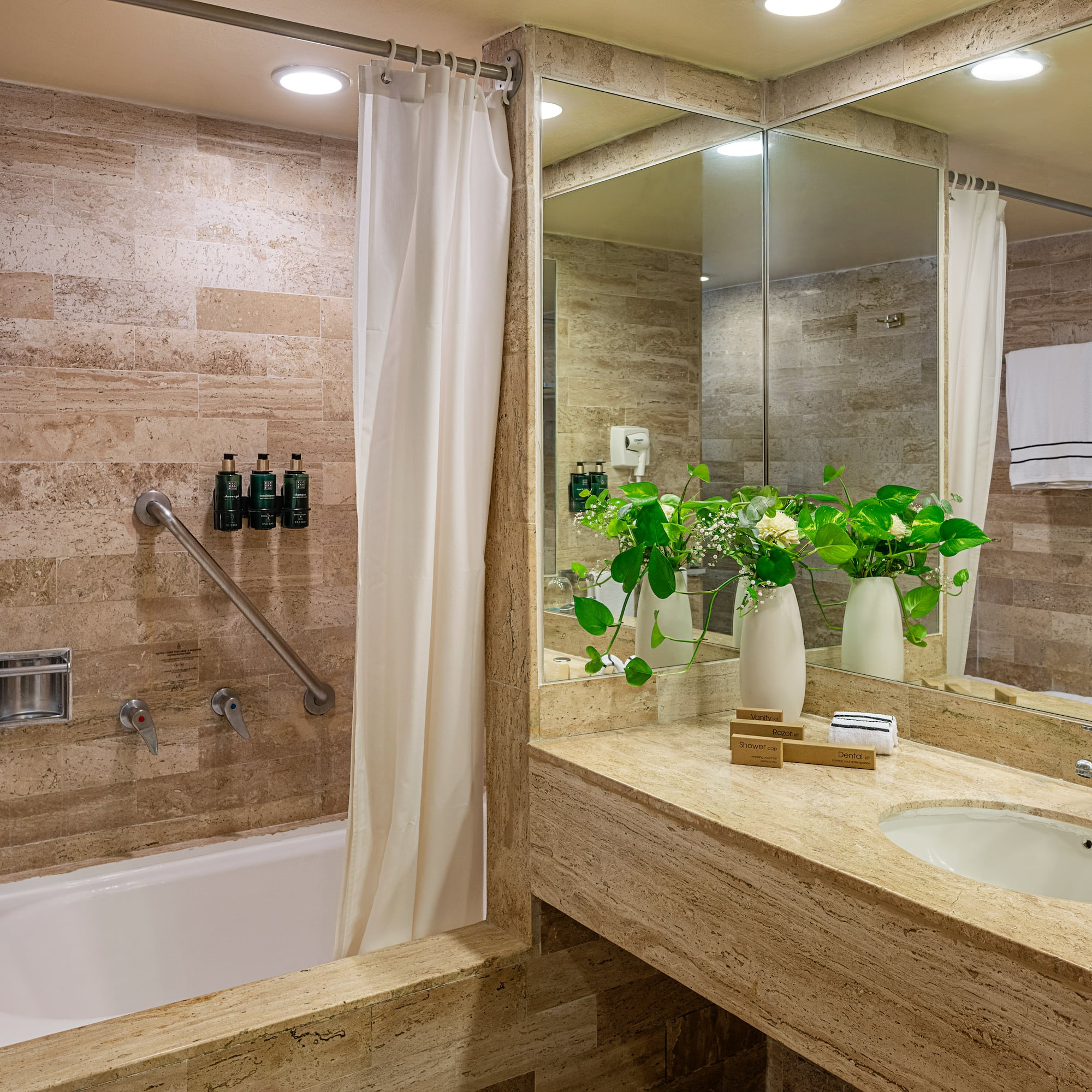 Stylish hotel bathroom with travertine tile, bathtub, grab bar, and vanity.