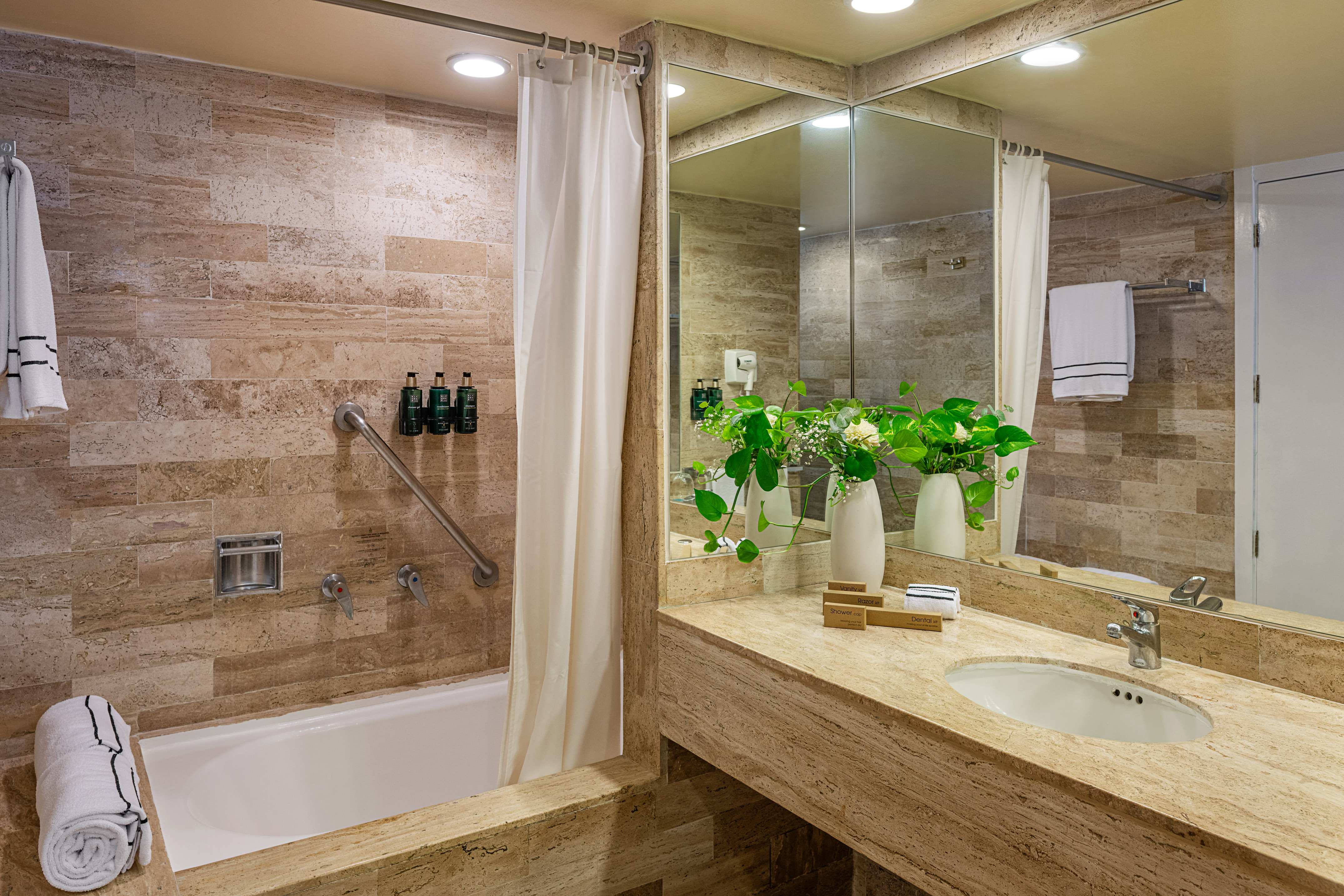 Stylish hotel bathroom with travertine tile, bathtub, grab bar, and vanity.