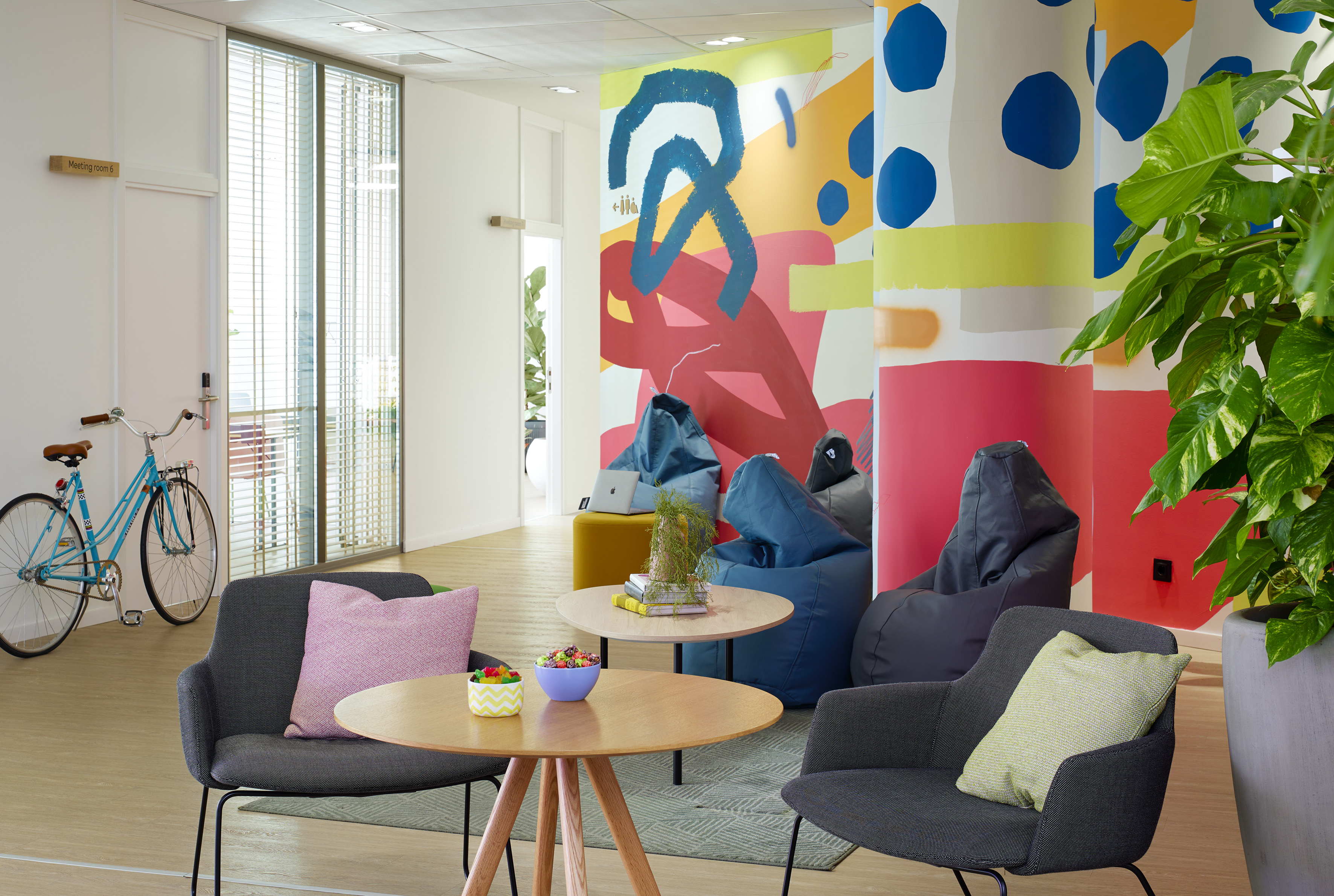 Colorful modern office lounge with abstract mural, comfortable seating, and bicycle.