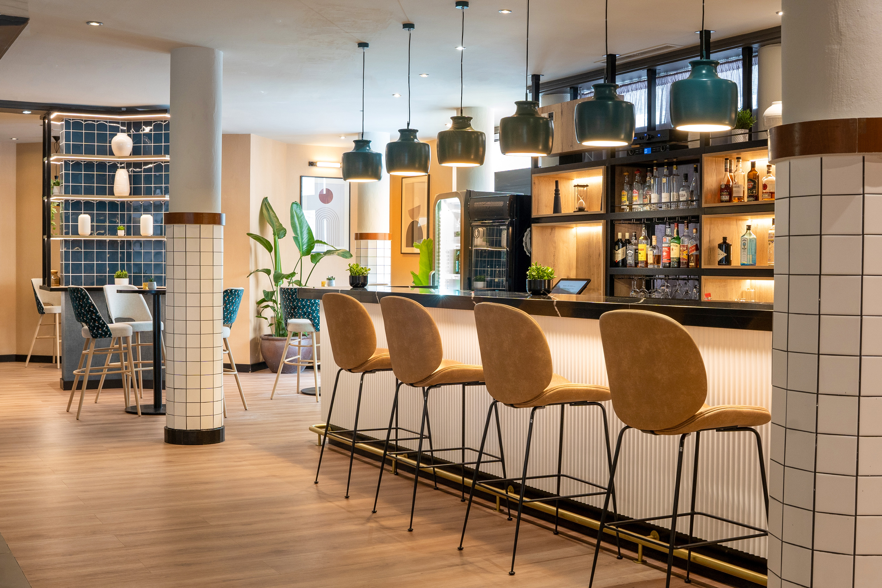 Modern bar with brown stools, dark teal pendant lights, and stocked shelves.