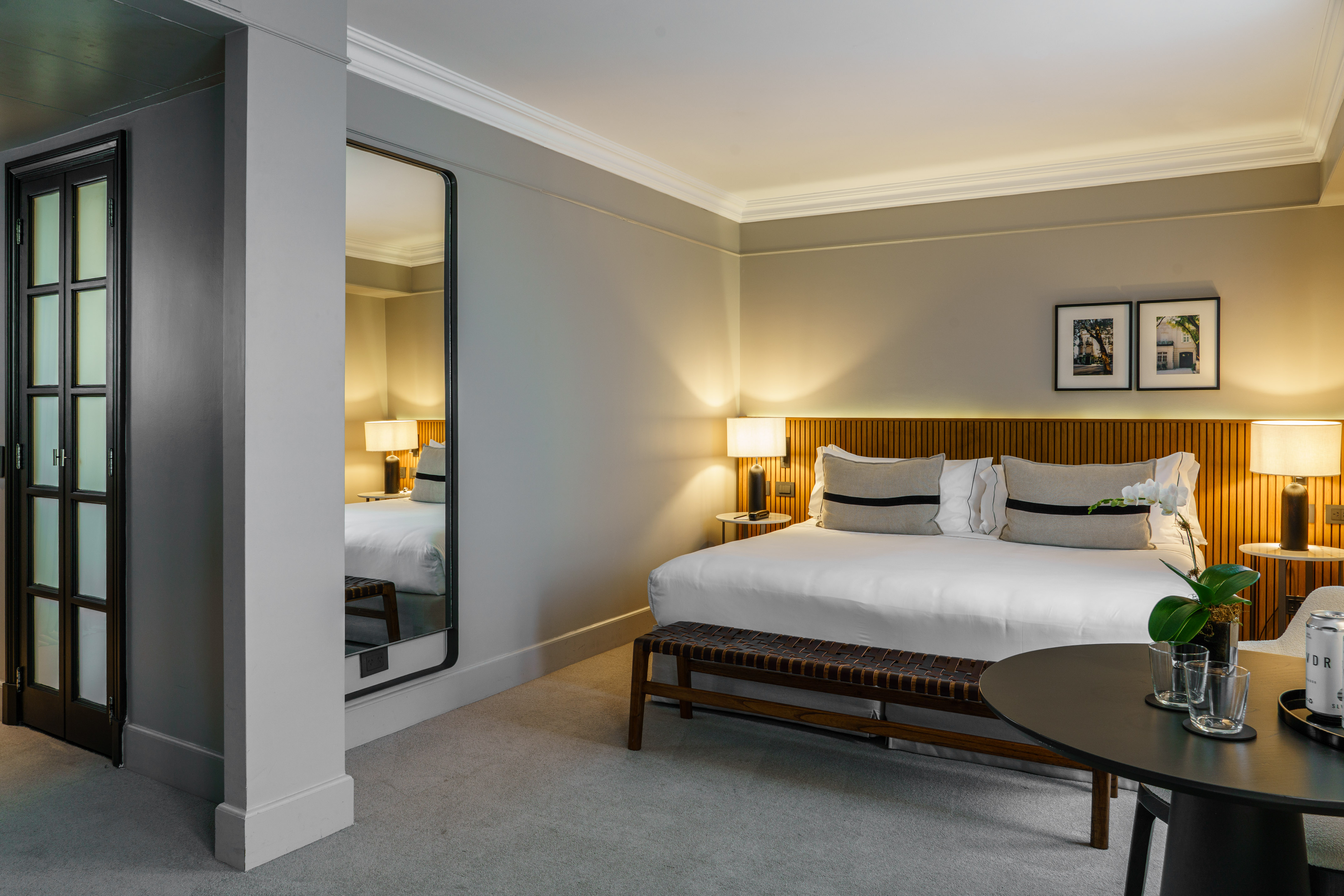 Luxury hotel bedroom with king bed, wooden headboard, and large mirror.