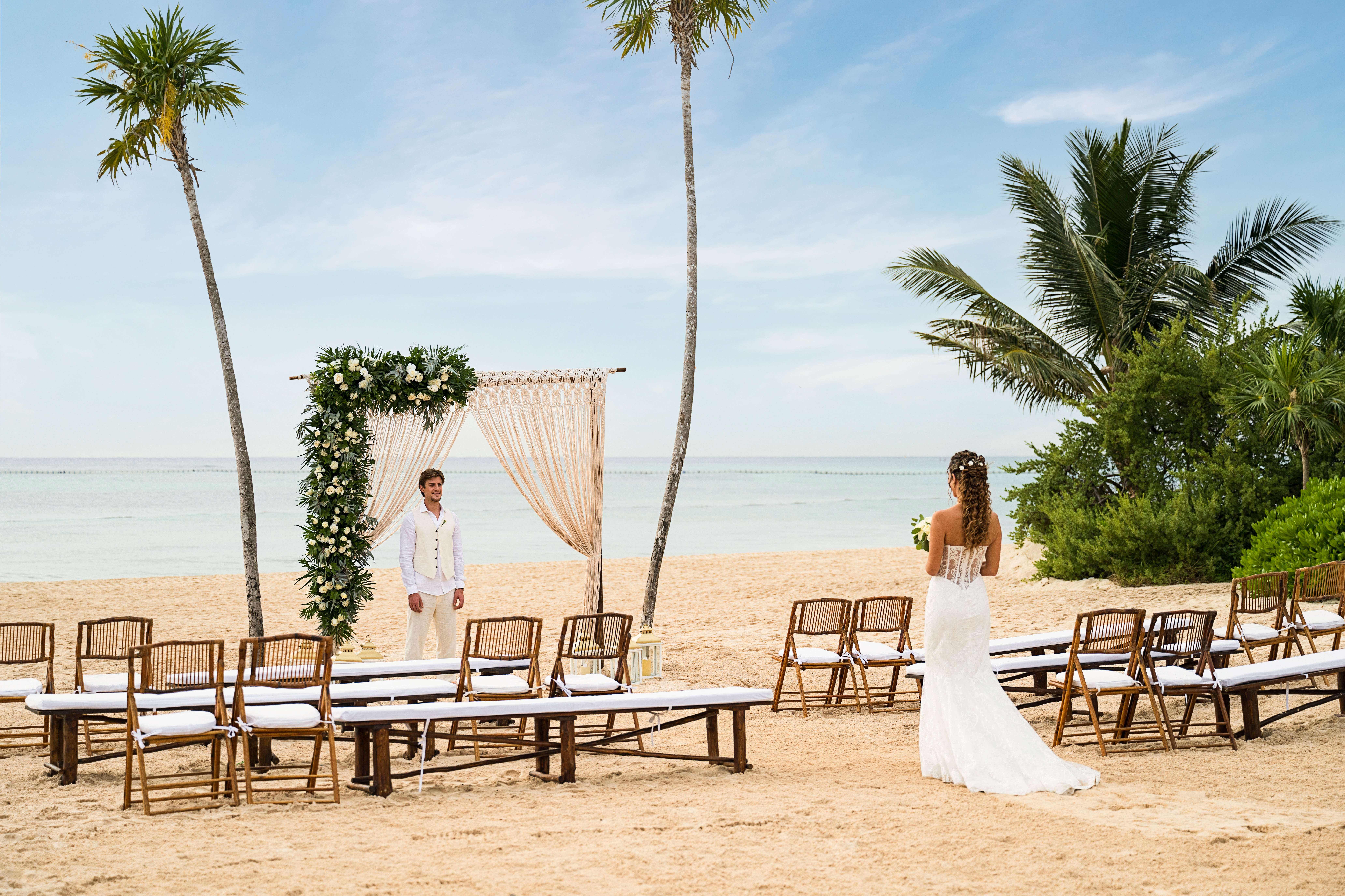 Bride and groom at tropical beach wedding ceremony with floral arch and ocean.