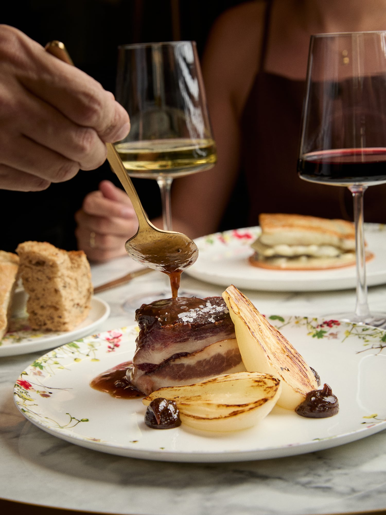 Hand pouring rich sauce on braised meat, roasted onions, fine dining.