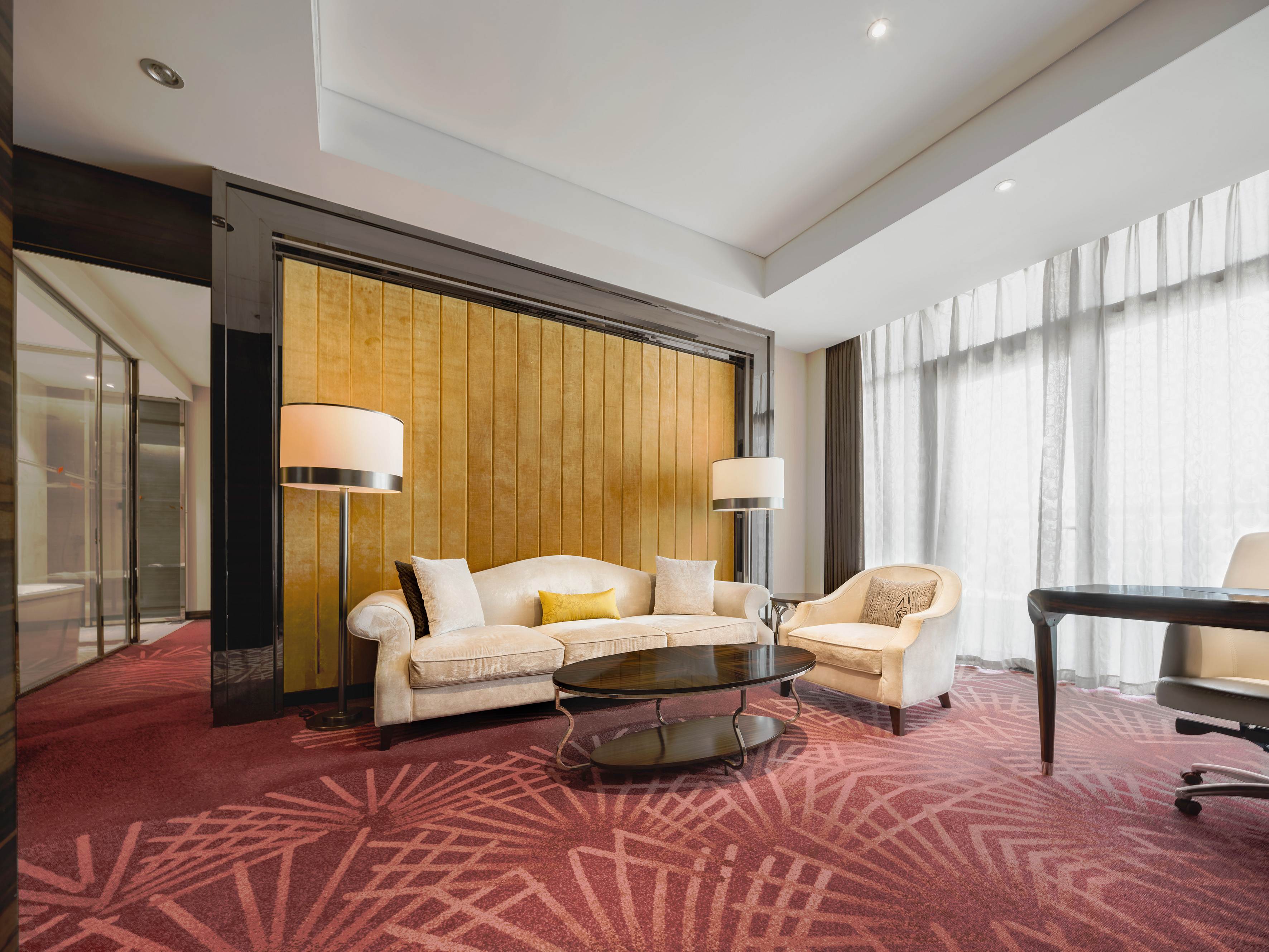 Luxurious hotel suite lounge with cream sofa, gold wall, and red patterned carpet.