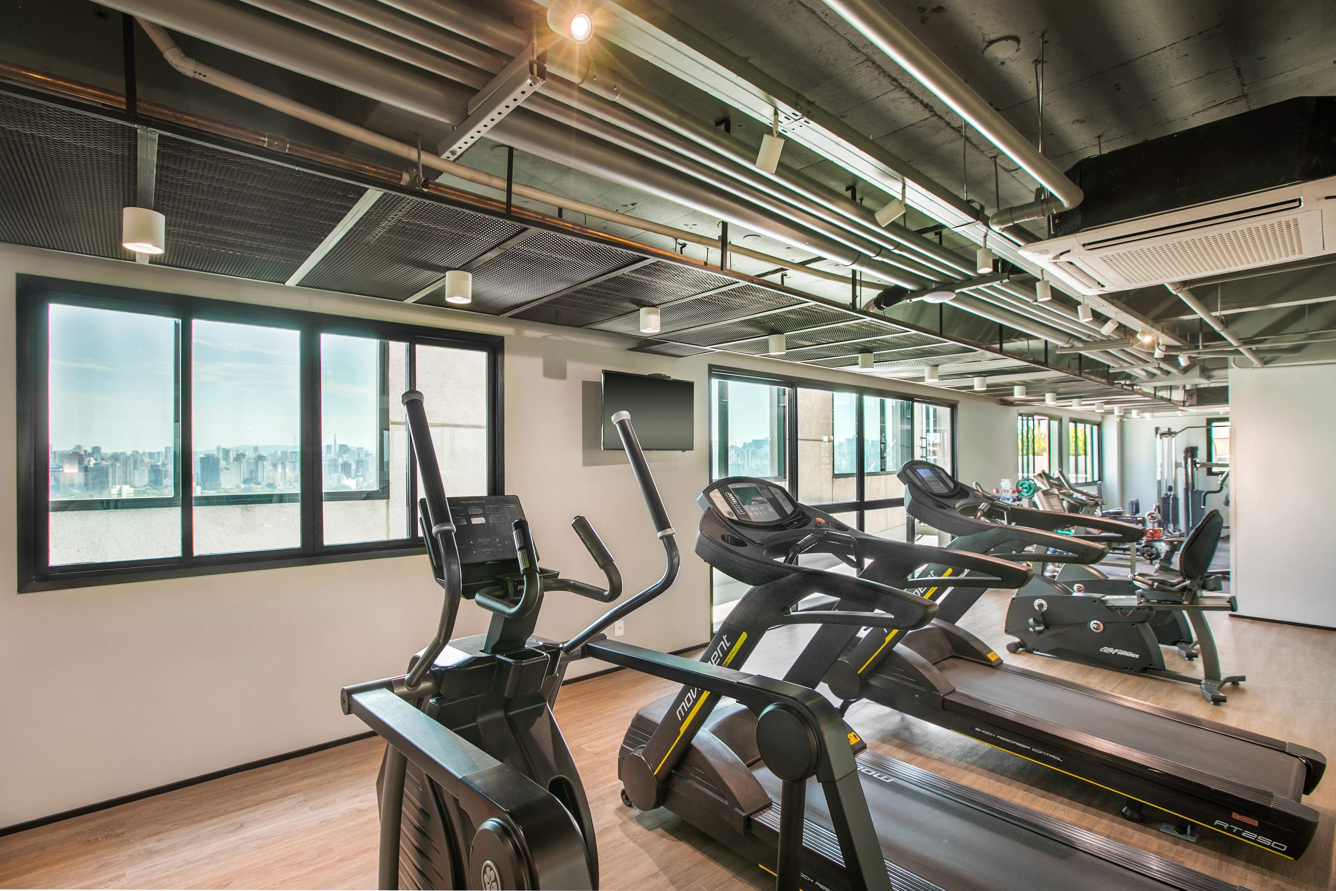 Modern gym with treadmills, elliptical, and city skyline view.
