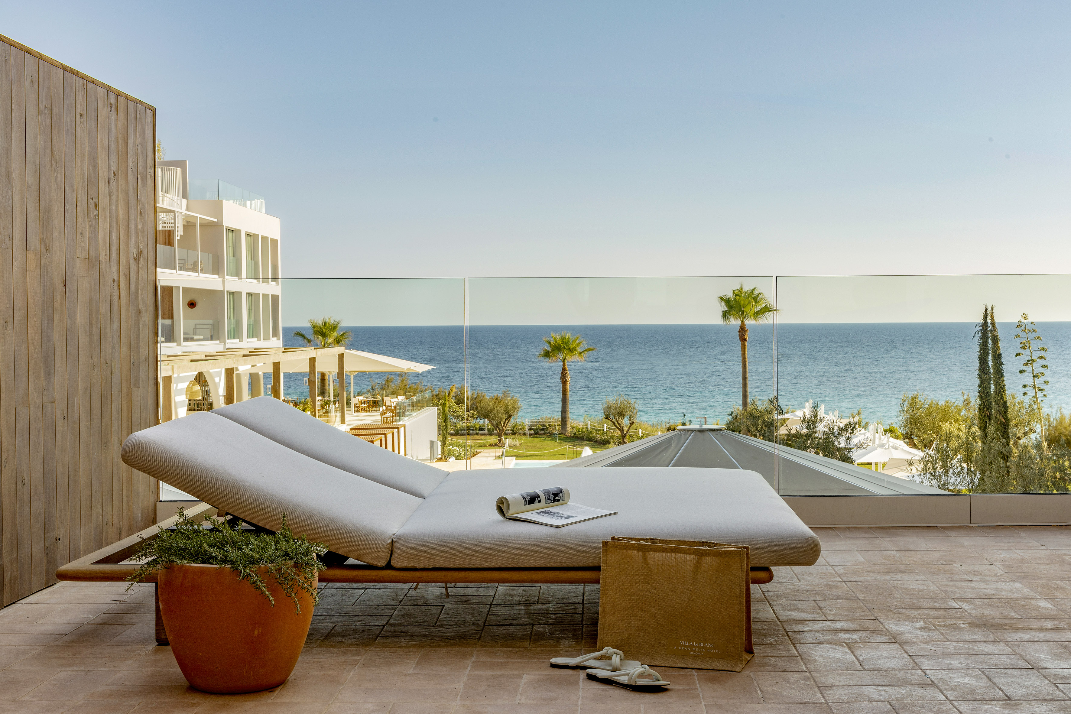 Oceanfront hotel balcony with daybed, sea view, and palm trees.