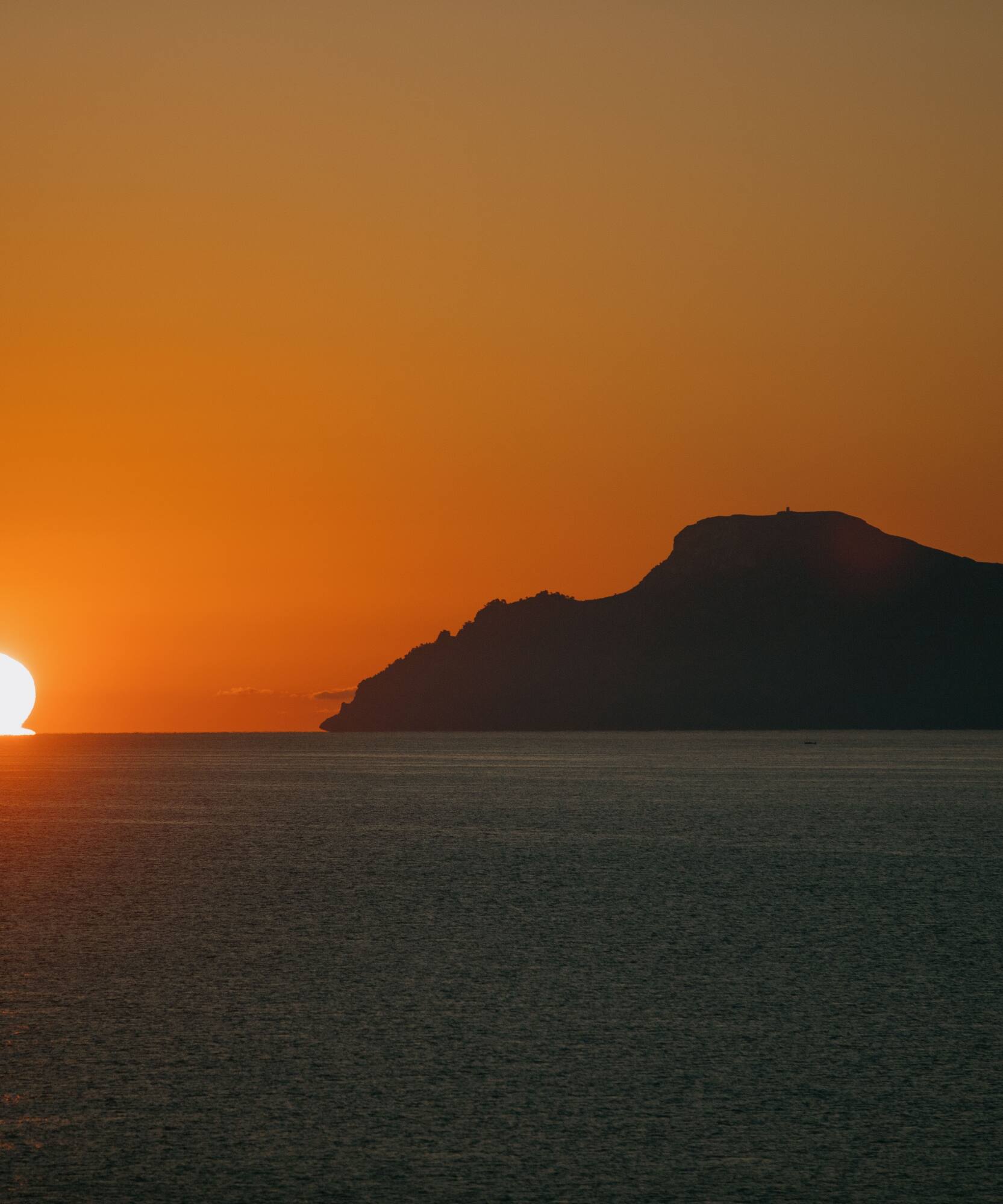 Puesta de sol naranja sobre el mar con silueta de montaña.