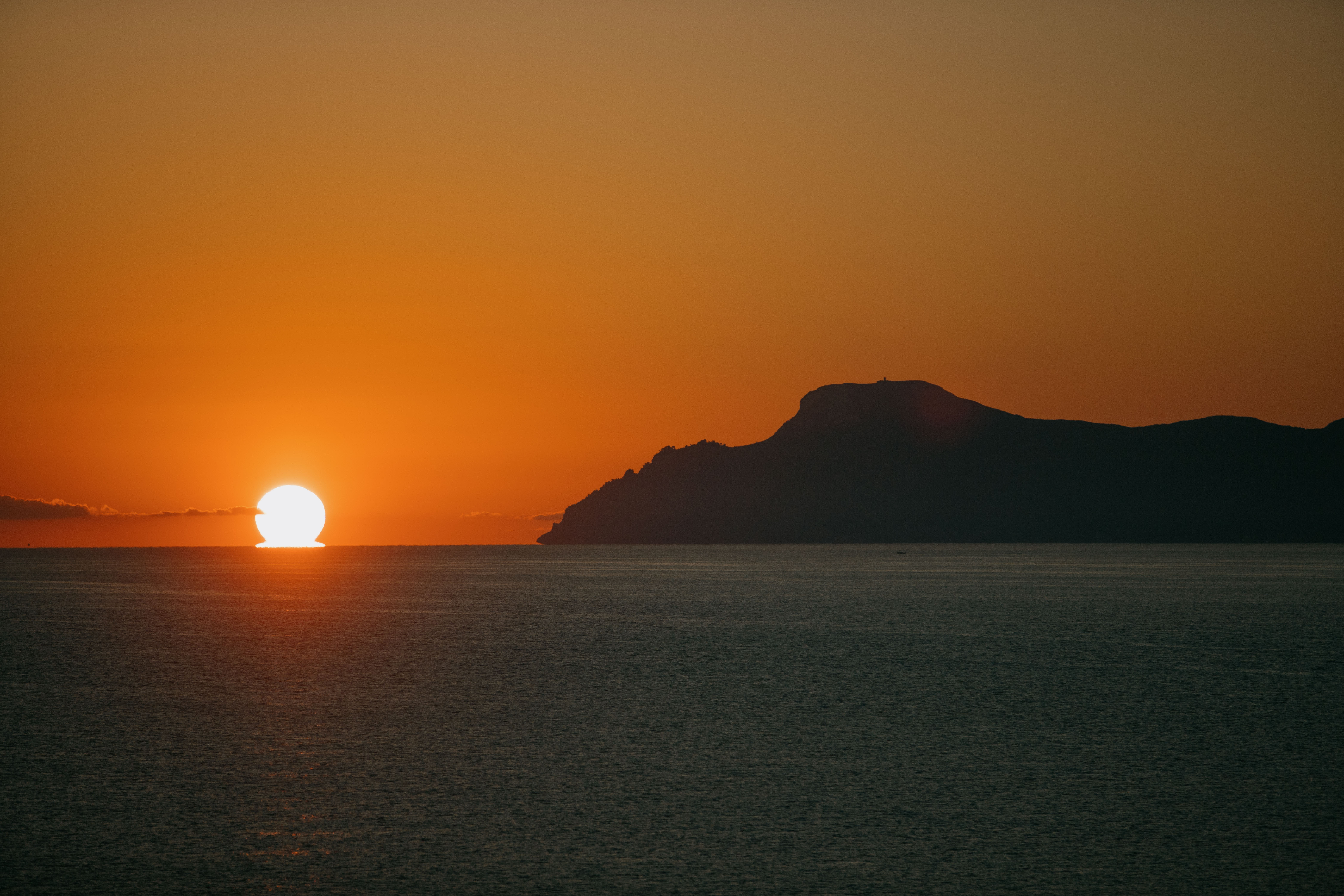 Puesta de sol naranja sobre el mar con silueta de montaña.