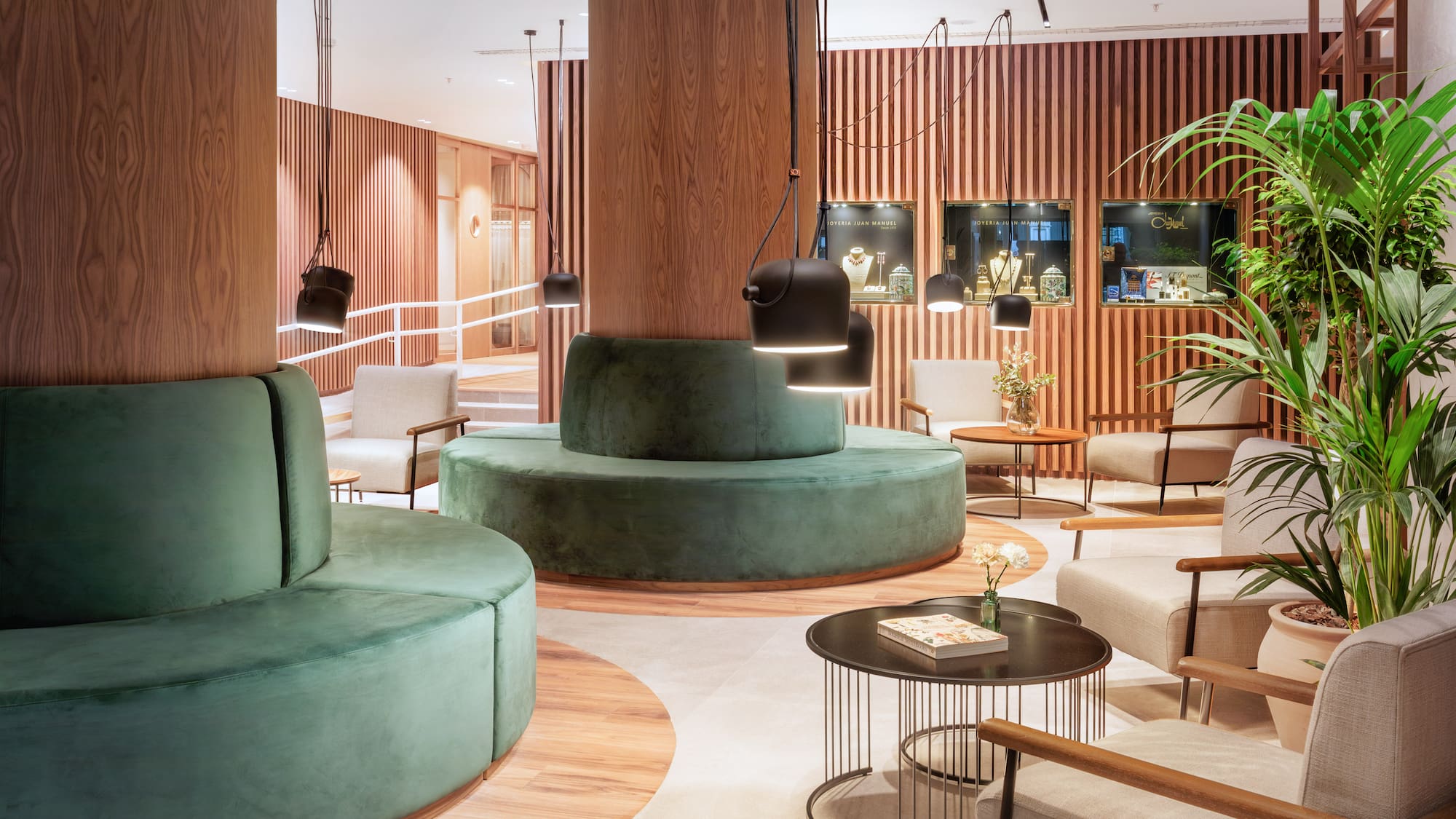 Modern lobby lounge with green velvet seating, wood panels, and pendant lights.