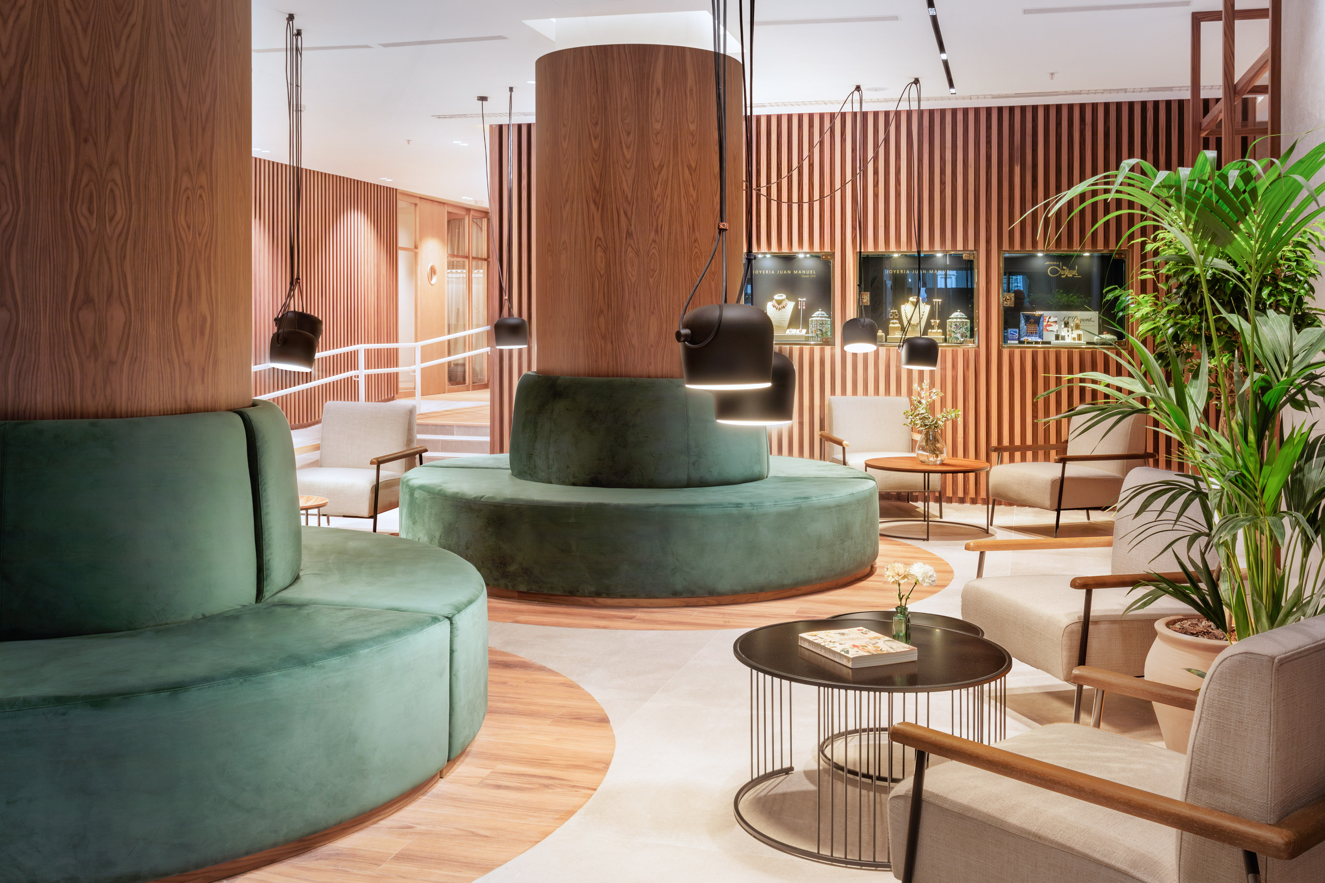 Modern lobby lounge with green velvet seating, wood panels, and pendant lights.
